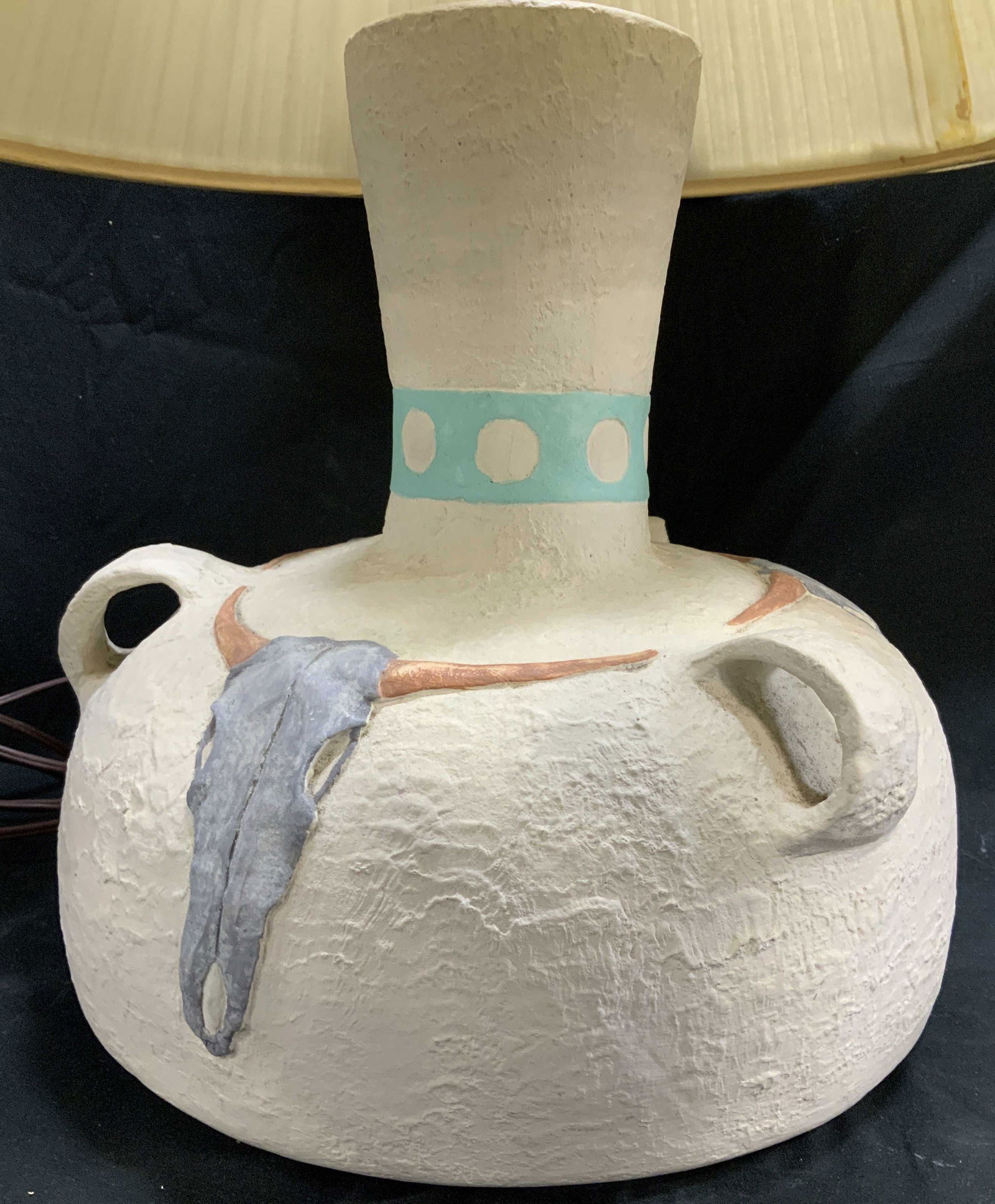 Southwestern Style Skull Motif Painted Table Lamp: Decorative ceramic table lamp features a round shape & hand painted skull motifs. Turquoise band with circle accents on neck of lamp. Textured finish. No visible signature or markings. Surface