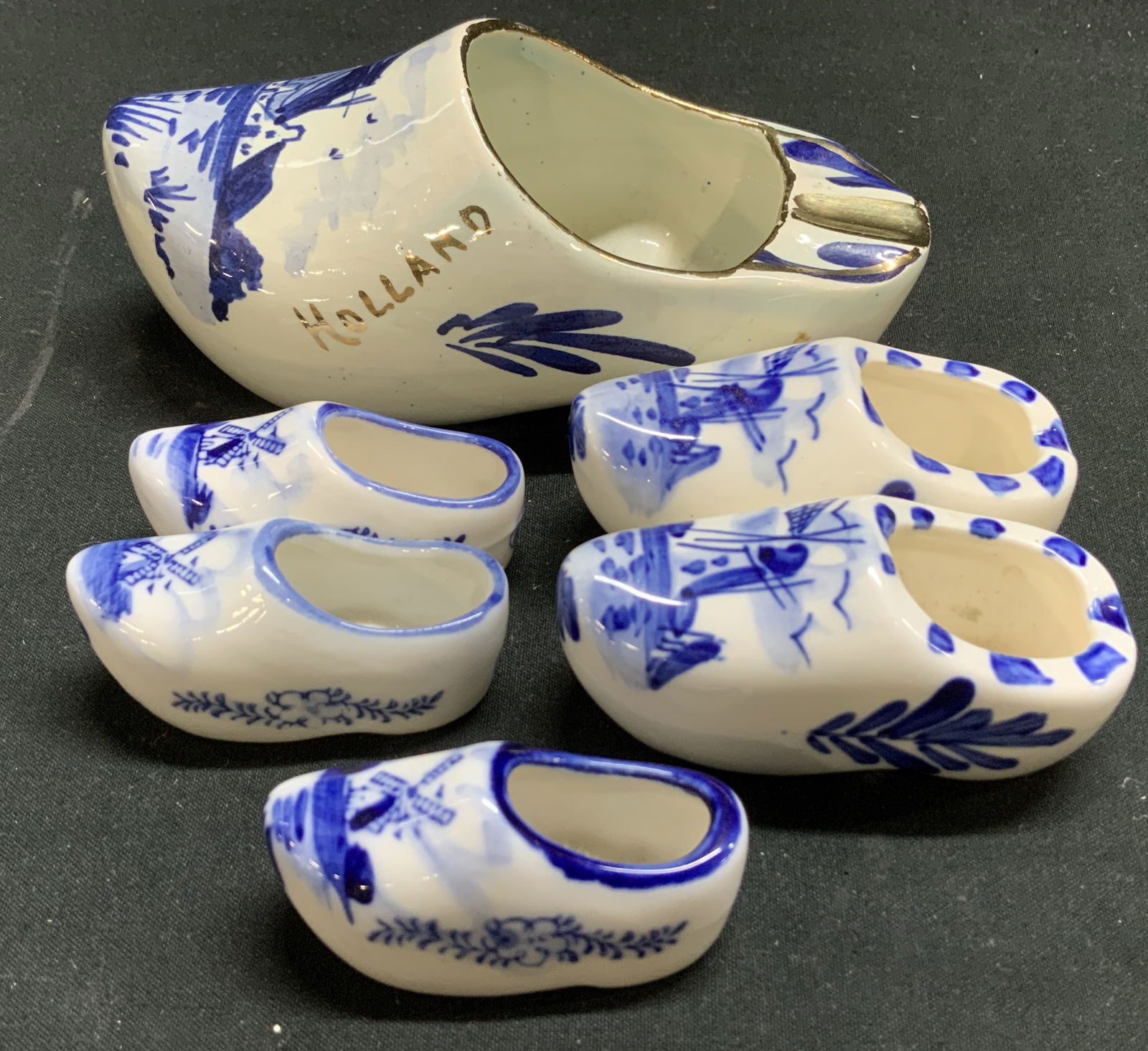 Lot 7 Delft Blue Mini Clog Shoes & Ashtray HOLLAND: Lot includes, 1 Delft Blue clog shoe serving as an ashtray & 6 miniature clog shoes. Pieces are ceramic & porcelain material. Hand painted floral & windmill motifs. Signed & marked on underside.
