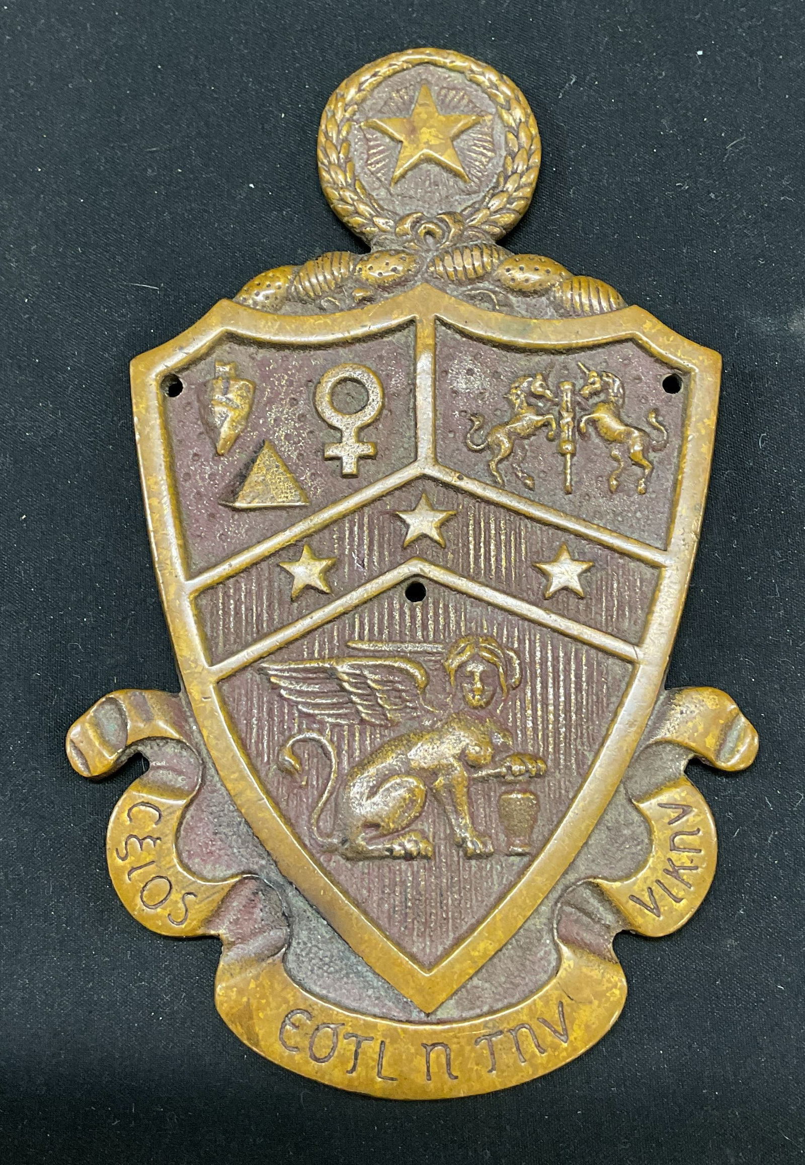 Coat Of Arms Metal Plaque: Coat of Arms metal plaque. Shield design. Cast metal plaque with vintage bronze patina. Features symbols including stars, torch, triangle, female, horses, and a griffin. Includes Greek lettering on a
