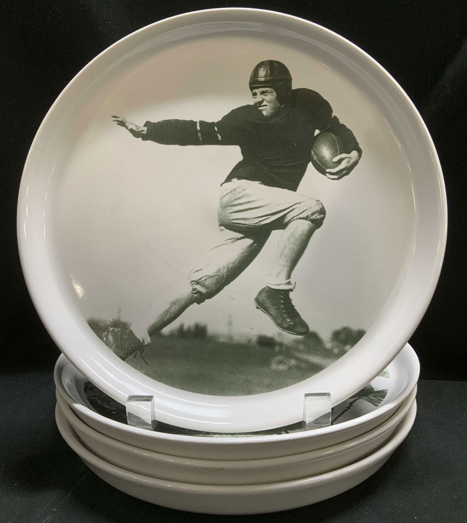 Set 4 Pottery Barn Football Collector Plates: Lot includes, set 4 of Pottery Barn football collector plates featuring a black-and-white images of players. Appears to be possible stoneware material. Signed & marked on underside. Reads, POTTERY BAR