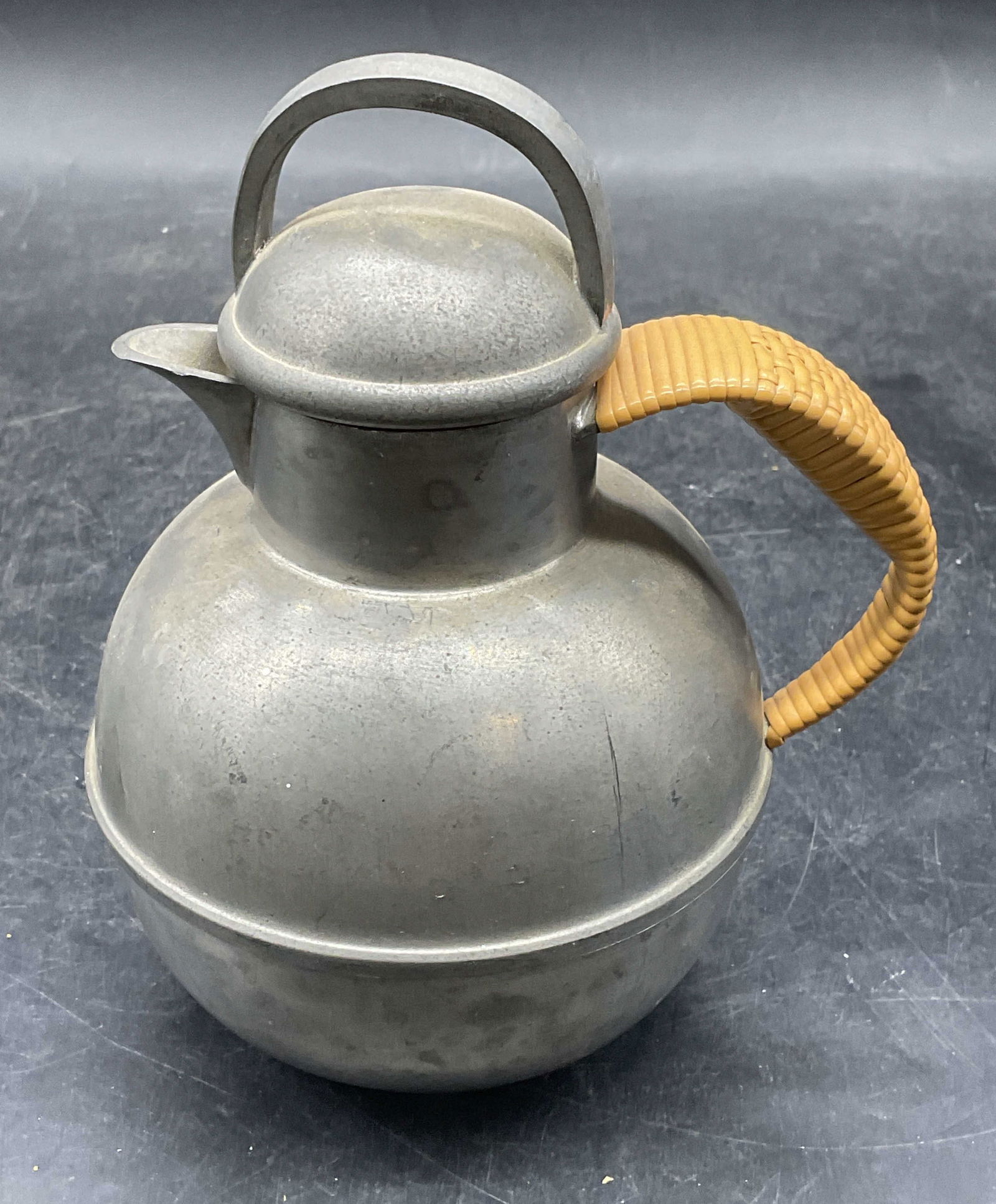 International Pewter Woven Handle Pitcher: International pewter pitcher with woven wicker style vinyl handle. Measures approx 4 x 5.75 inches. Wear including scratching and patina. International pewter pitcher, pewter pitcher, vintage pitcher,