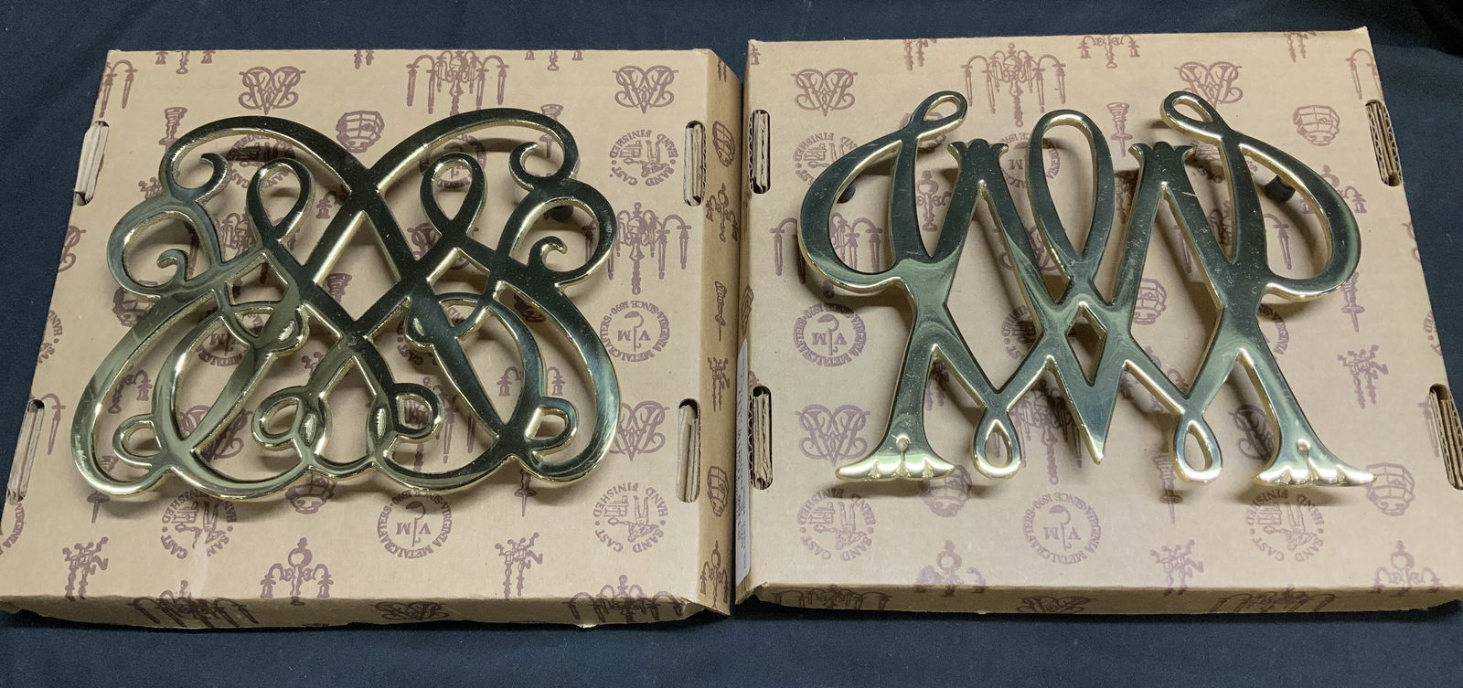 Lot2 Virginia Metal Crafters 1983 Brass Trivets Bx: Lot includes, 2 Virginia Metalcrafters polished brass trivets. William Rex Trivet, WM & Mary Trivet. Comes with original box. Signed & marked. Reads, VIRGINIA METALCRAFTERS. 1983 THE COLONIAL WILLIAMS