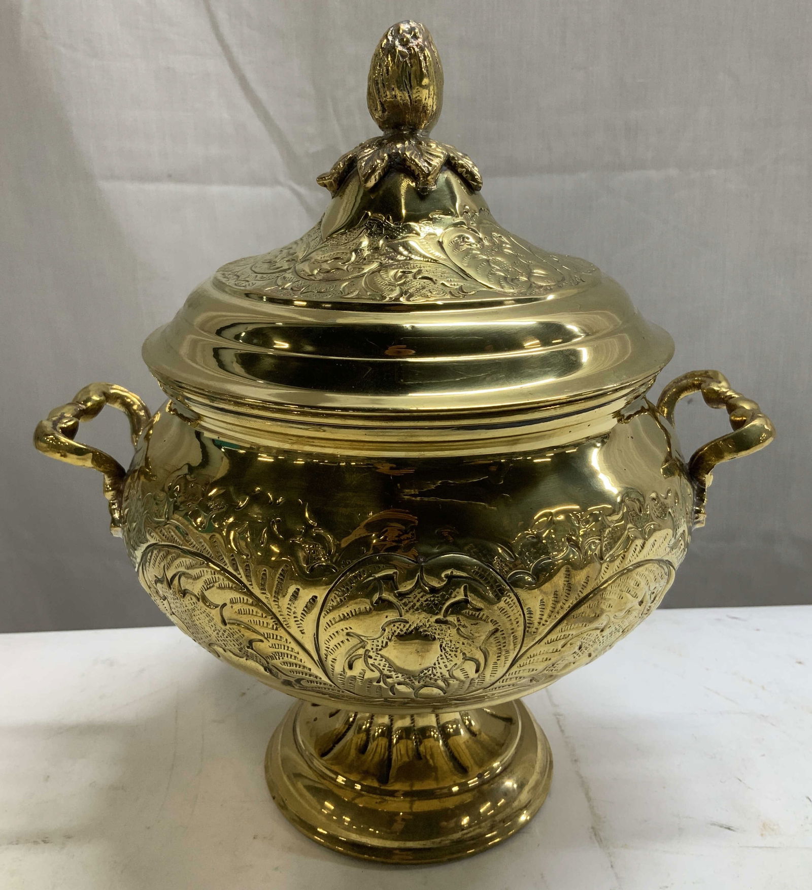 Vtg Brass Plated Embossed Pedestal Pot INDIA: Vintage pedestal pot features intricate embossed leaf like motifs. Decorative handles & leaf shaped finial. Pot is brass/gold plated. Signed & marked on underside. Reads, MADE IN INDIA. Surface wear c
