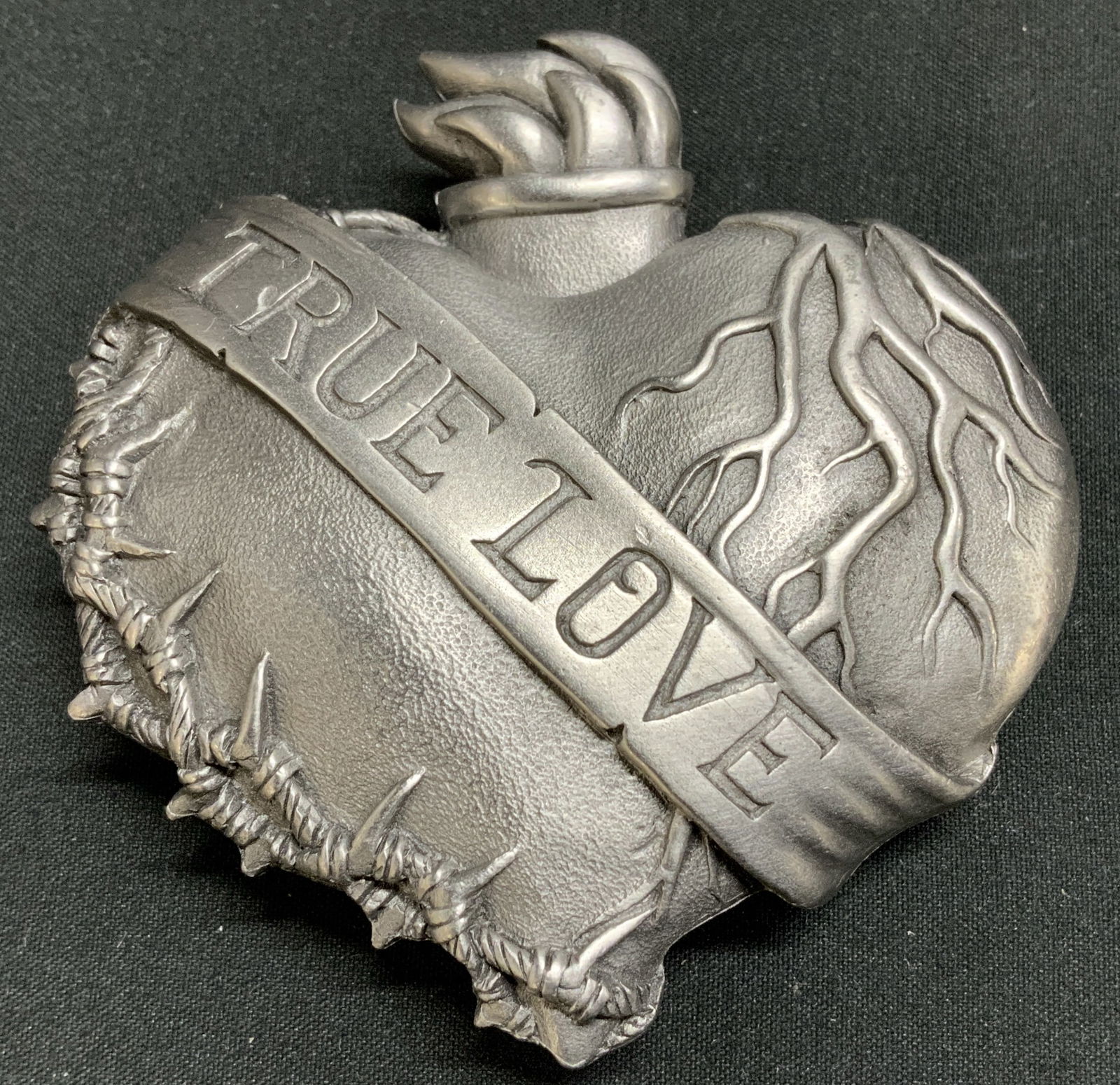 2006 Bergamot True Love Flaming Heart Buckle: Buckle is heart-shaped & features flames emerging from the top. Banner crosses center of heart w words that reads, TRUE LOVE. Piece appears to be pewter. Signed & marked. Reads, 2006 BERGAMOT. DELAVAN
