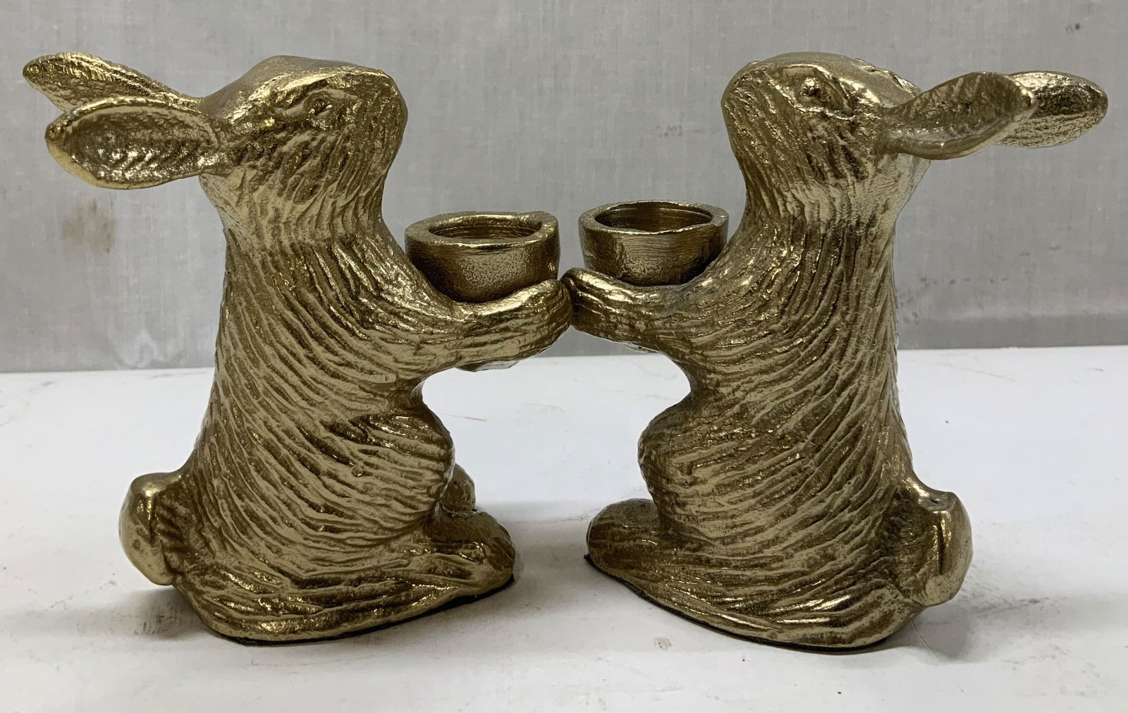Pair Gold Toned Metal Rabbit Candle Holders: Lot includes, a pair of gold toned metal rabbit candle holders. Textured details on rabbits. No visible signature or markings. Surface wear consistent to age, use & exposure. Measurements: length 2.6i