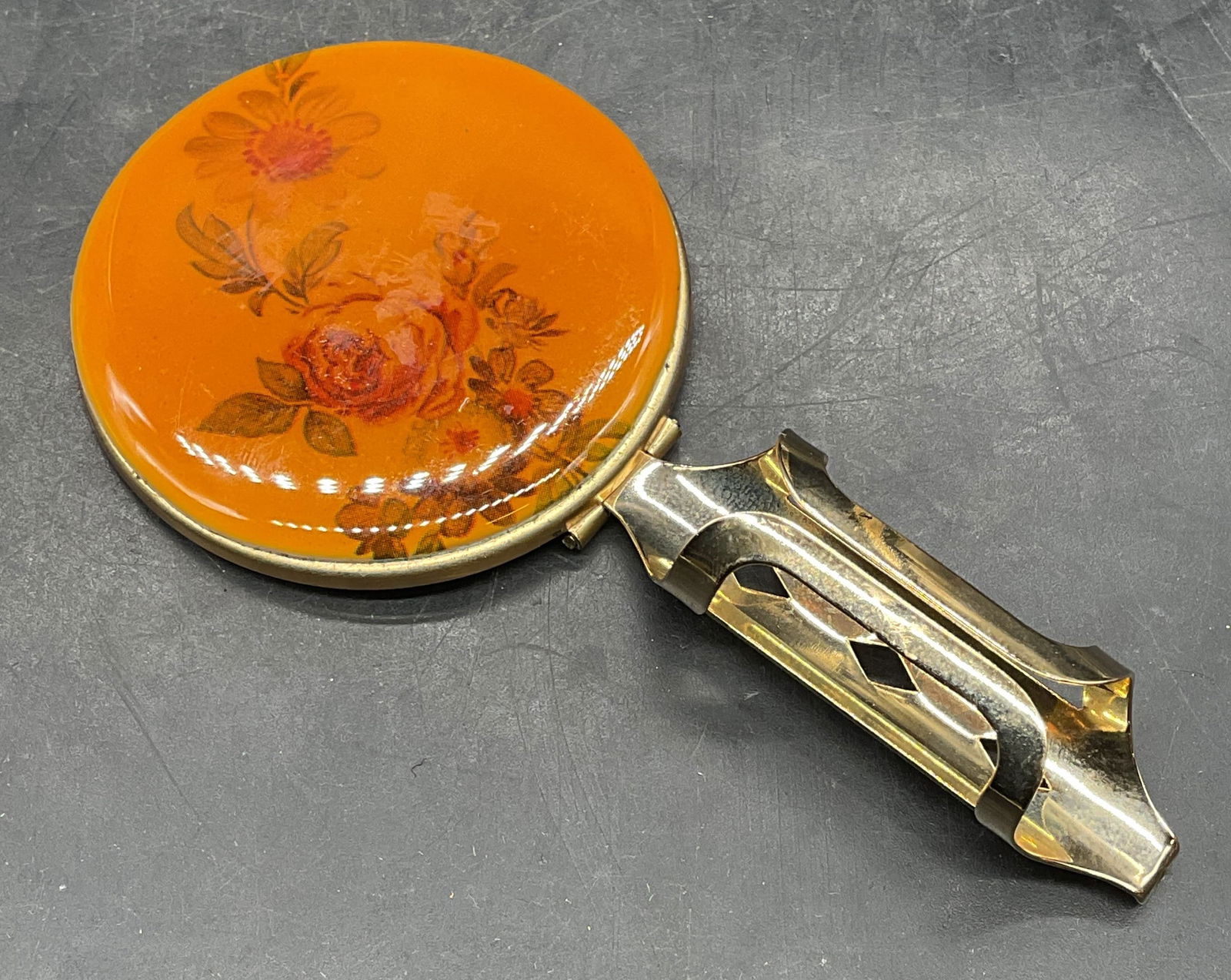 Vintage Gold Tone Floral Lipstick Holder Mirror: Vintage lipstick holder and hand mirror. Hinged. Floral print cover with resin. Measures approx 4.25 x 2. Wear including yellowing. Property of opera singers estate from the renowned and opulent