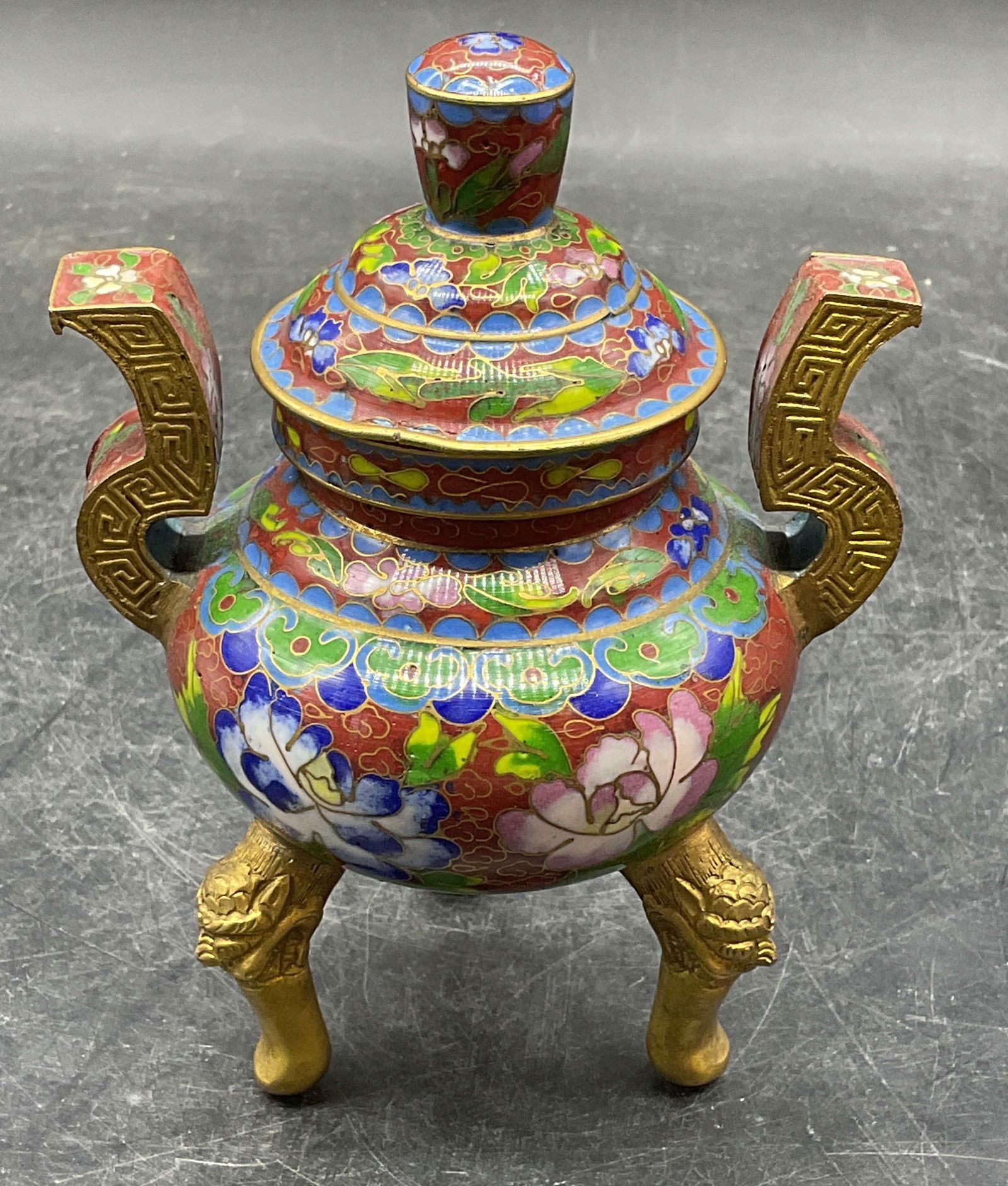 Asian Gilt Cloisonne Footed Incense Burner: Asian gilt cloisonne enameled incense burner. Lidded. Tripod base with foo dog design. Floral design on bowl. Measures approx 4 x 3 x 5.5 inches. Wear including loss to gilt and scratching.