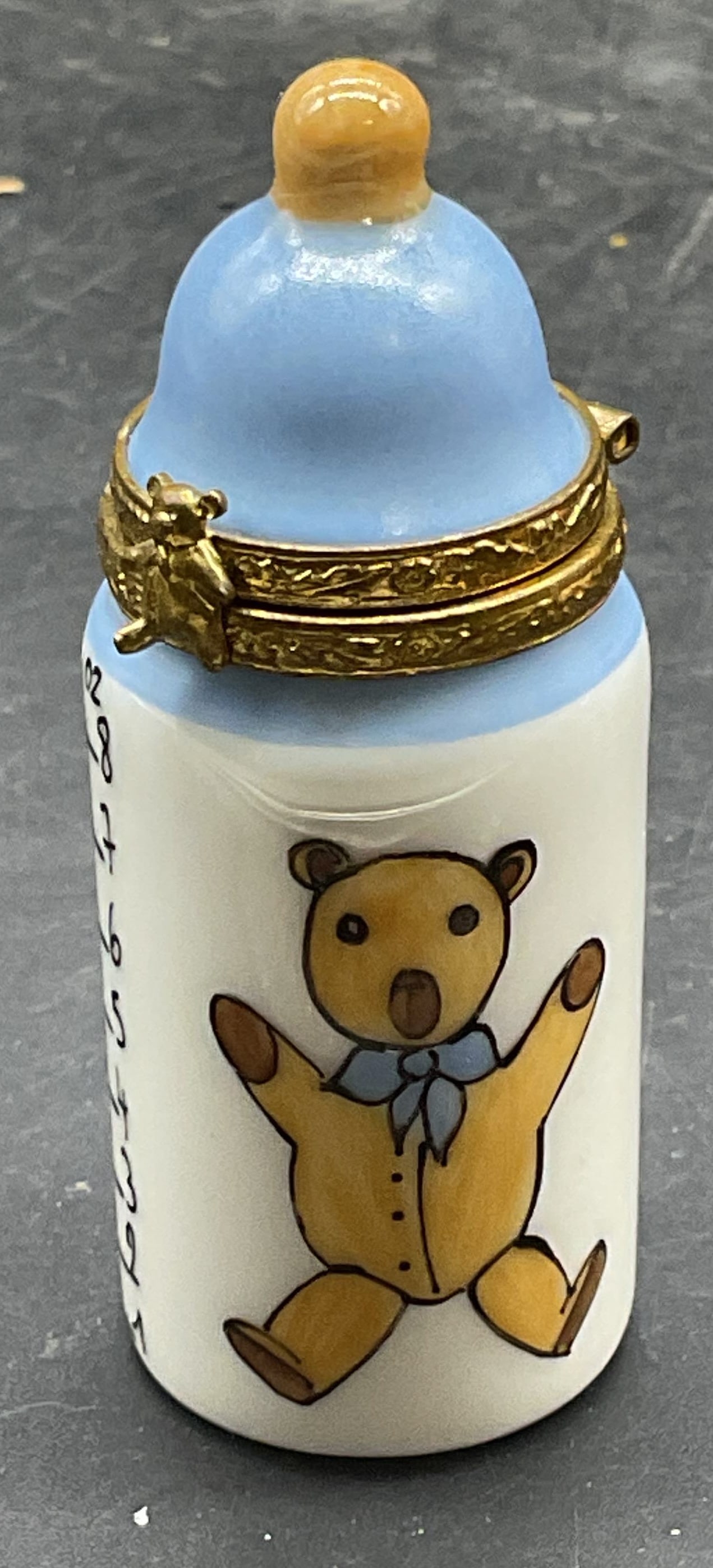 Limoges Porcelain Baby Bottle Trinket Box France: Vintage Limoges porcelain baby bottle trinket box in blue with Teddy bear motif. Hand painted. Signed. Made in France. Measures approx 2.5 x 1 inches. Lid previously reattached. Limoges trinket box, p