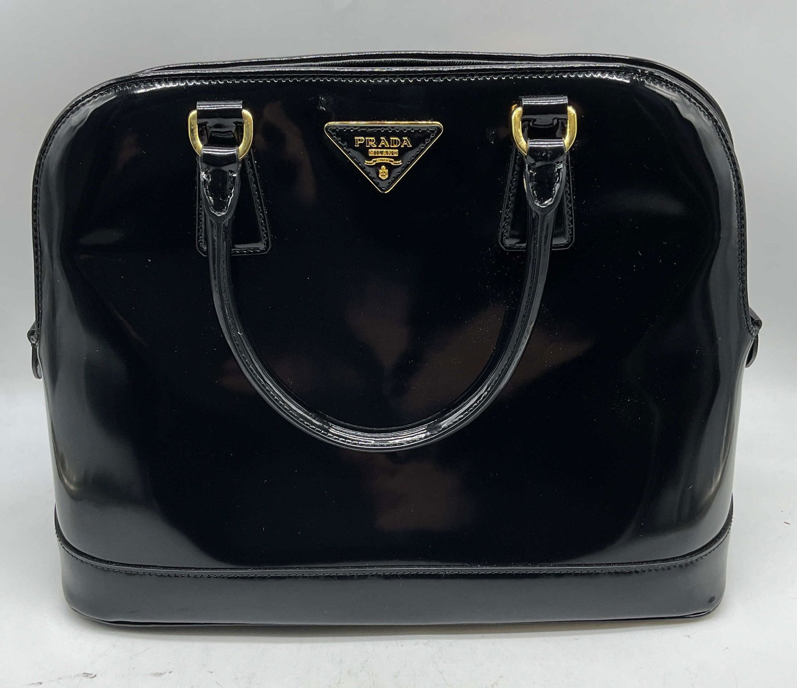 Prada Black Patent Leather Handbag, Italy: Prada black patent leather handbag. Signed on exterior and interior plaque. Made in Italy. Patent leather outer and leather lined interior. Top snap closure. 3 interior zippered pockets and 2 slip poc