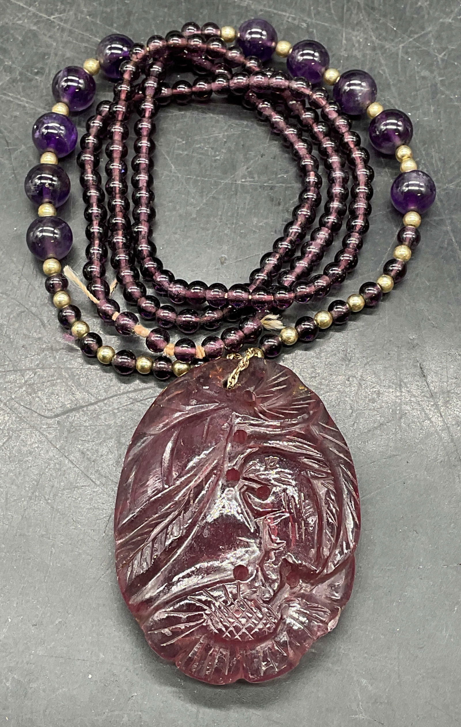 Carved Amethyst & Gold Pendant Necklace: Vintage amethyst beaded necklace with carved amethyst floral and rabbit motif pendant. Gold accent beads. Tested for gold, purity unknown. Drop length approx 12.75 inches. Pendant measures