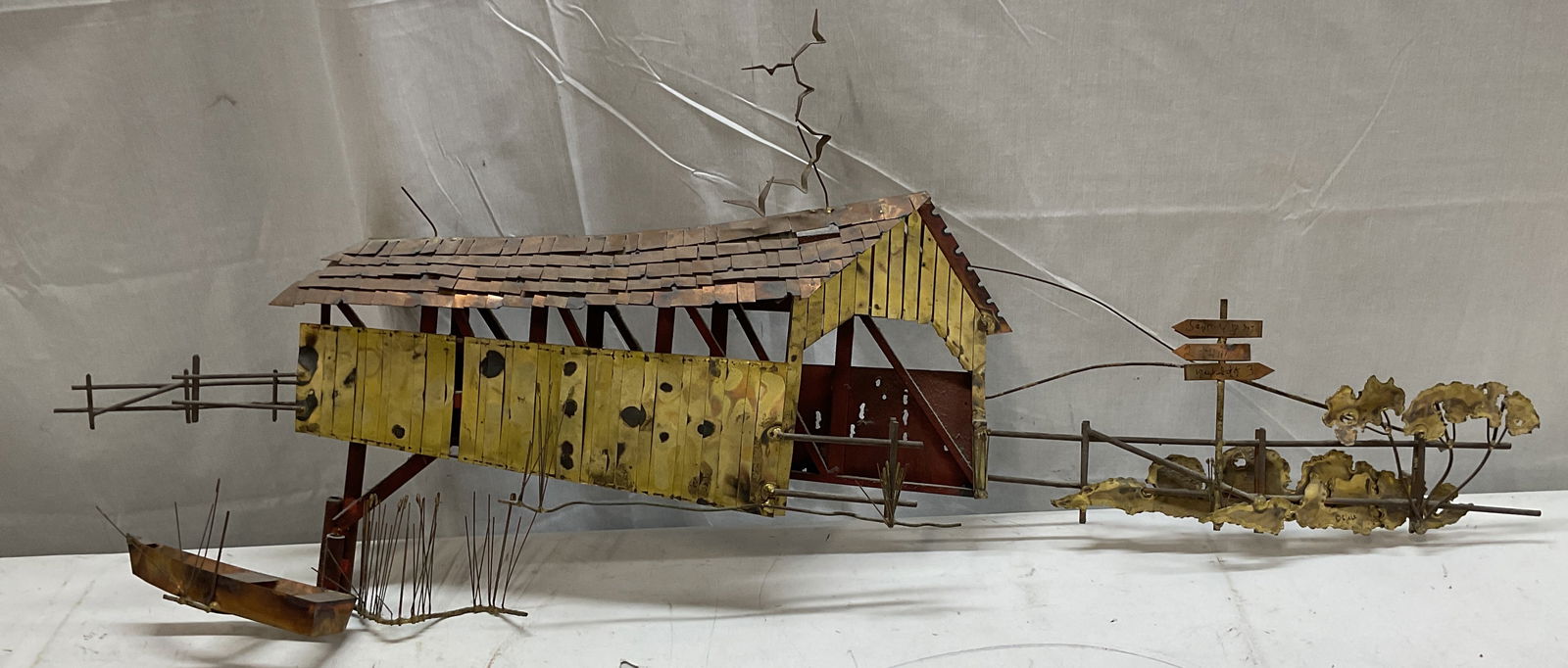 MCM Curtis Jere Covered Bridge Metal Wall Art 44in: Mid century modern signed Curtis Jere sculpted metal wall hanging. Covered bridge with rowboat and road signed. Measures approx. 44 inches wide, 20 inches tall, 4 inches deep. Wear including patina, s
