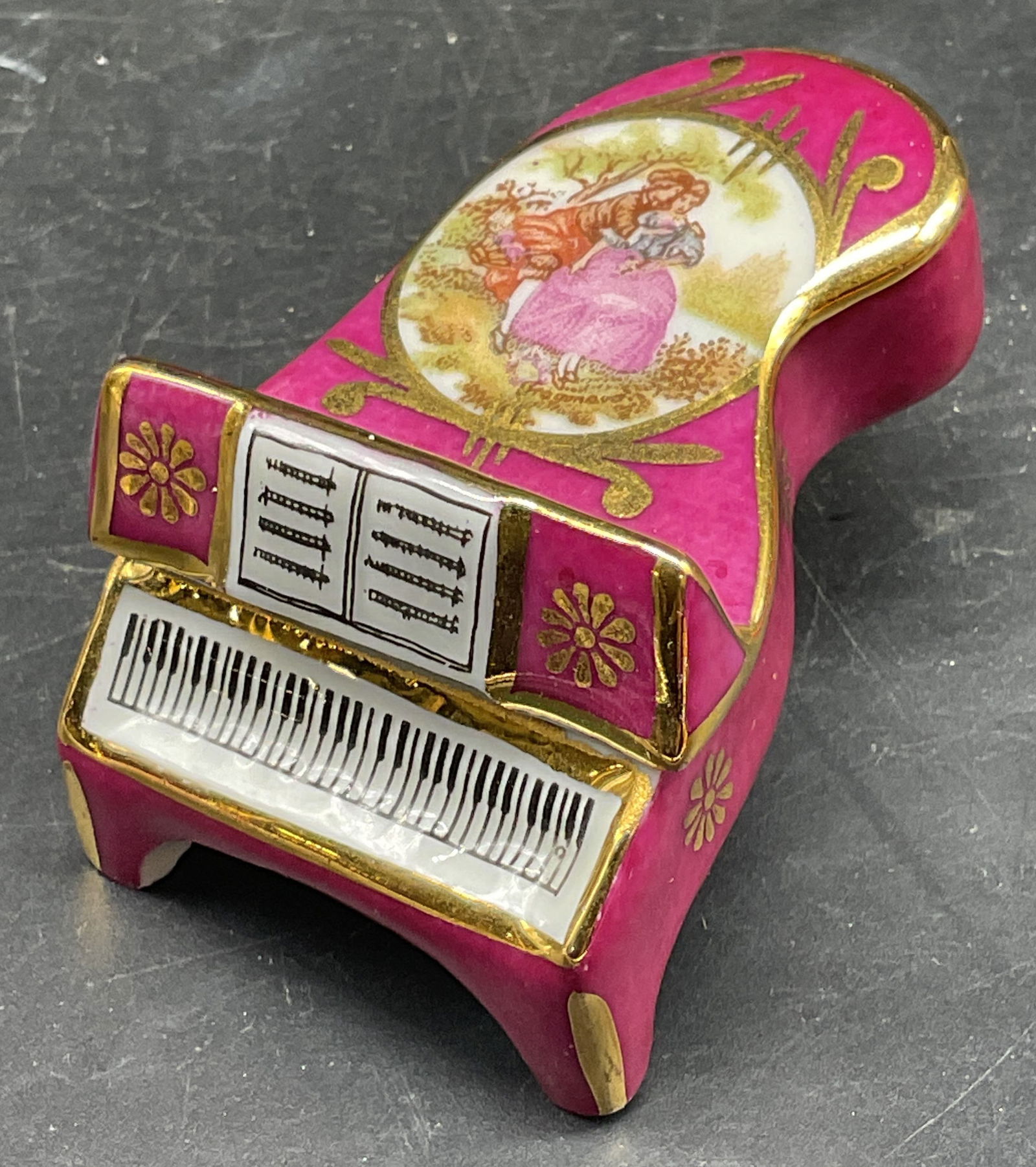 Limoges Porcelain Piano Trinket Box, France: Limoges hand painted and gilt porcelain piano trinket box with courting couple scene. Measures approx. 2.5 x 1.5 x 1.25 inches. Signed, made in France. Some scratching. Limoges trinket box, piano