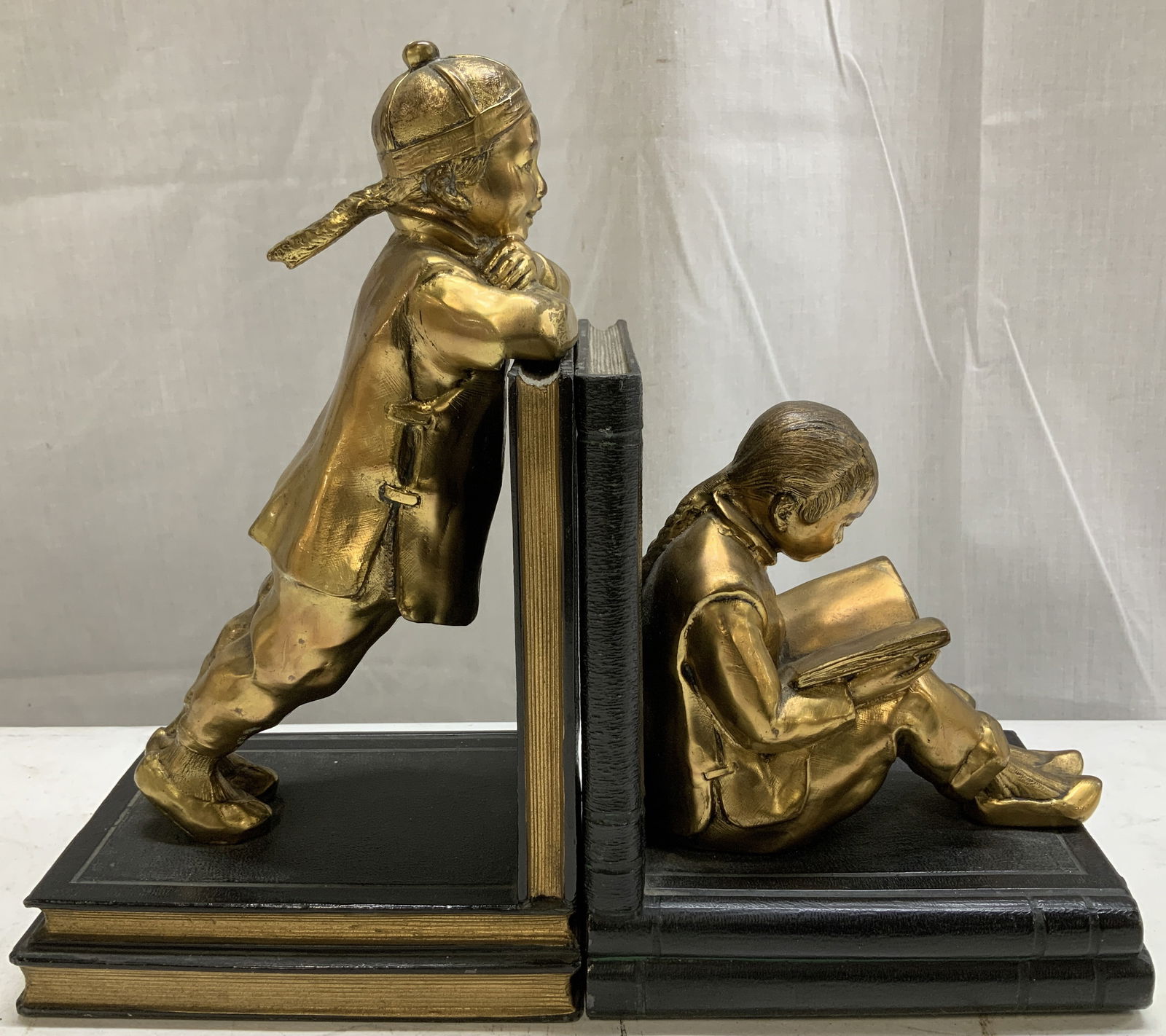 Pair Vtg Gilt Metal Asian Children Bookends: Lot includes, a pair of vintage gilt metal bookends depicting two children in traditional Asian attire. One stands leaning against a book, while the other sits & read. Gilt accents. Pieces have some w