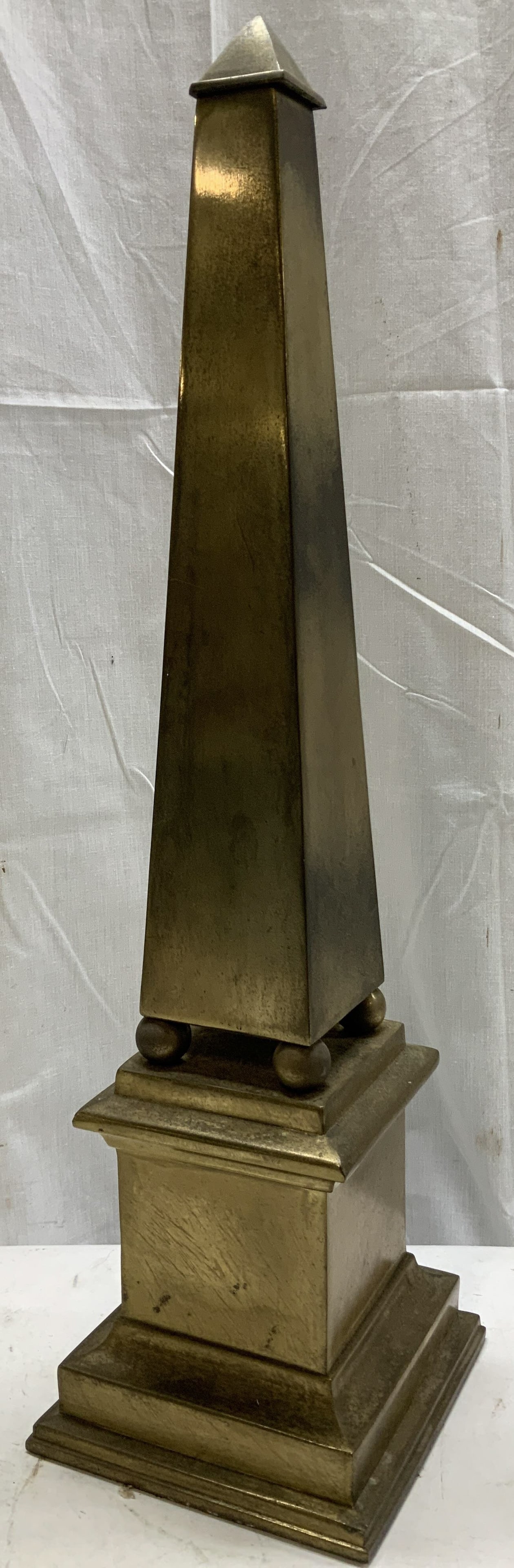Gimbels Large Vtg Solid Brass Obelisk 21.5in: Lot includes, large vintage obelisk features 4 spherical ball supports, which sit stop a square, stepped pedestal base. Brass material. Surface wear consistent to age, use & exposure. Signed & marked
