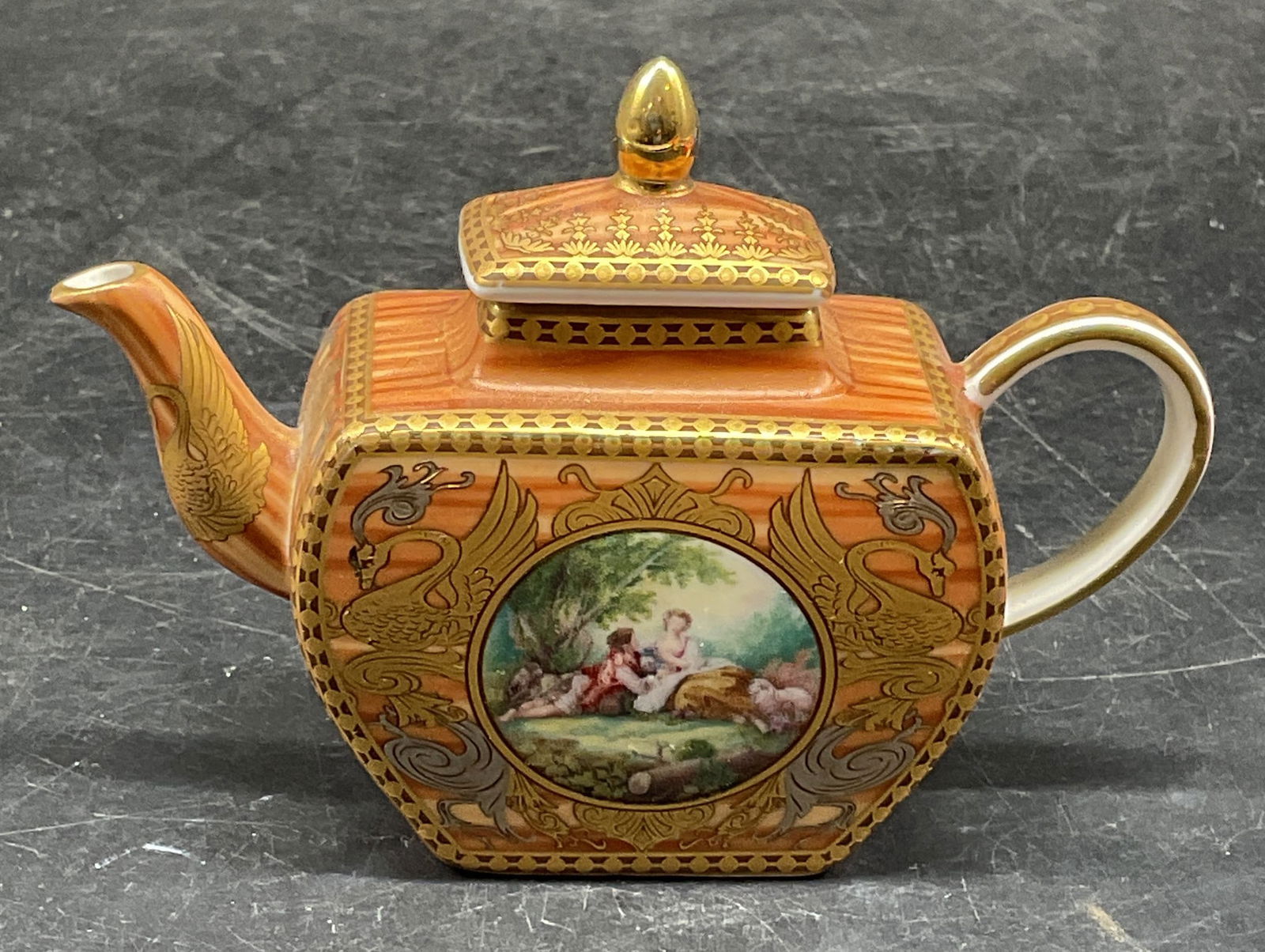 Orchid Miniature Gilt Porcelain Teapot: Signed Orchid miniature teapot. Courting couple motif with hand painted gilt decoration. Measures approx. 4.5 x 1.5 x 3 inches. Some scratching. Miniature teapot, teapot figurine, porcelain teapot, or