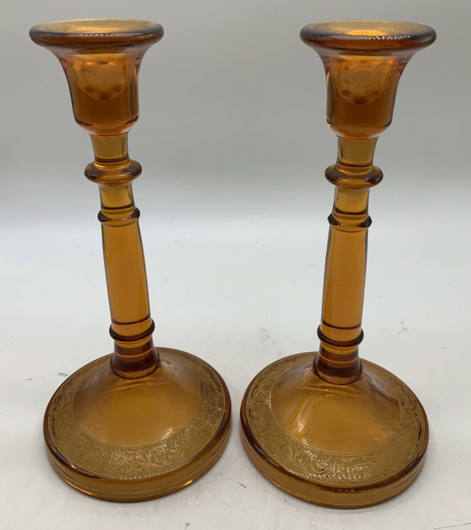Pair Vtg Cambridge Glass Candlestick Holders: Lot includes, a pair of vintage Cambridge glass candlestick holders features gilt encrusted detailing on base. Round base. Surface wear consistent to age, use & exposure. Measurements: length
