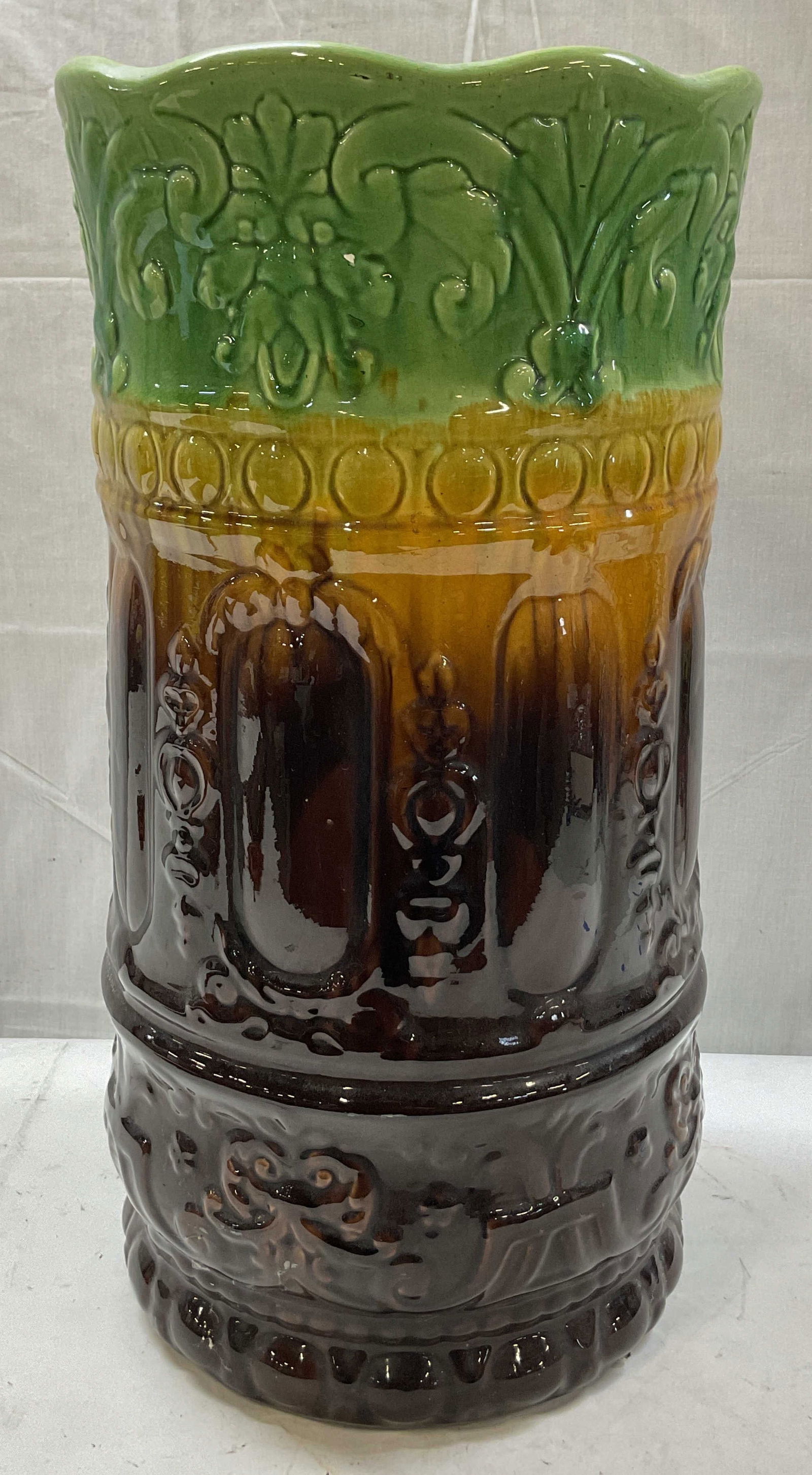 Vintage Pottery Umbrella Stand 20.5in: Vintage ceramic pottery umbrella stand. Scalloped edges. Embossed floral and scroll motifs. Hand painted green, yellow, and brown. Measures ht approx 20.5 inches diam approx 10.5 inches. Crack on side