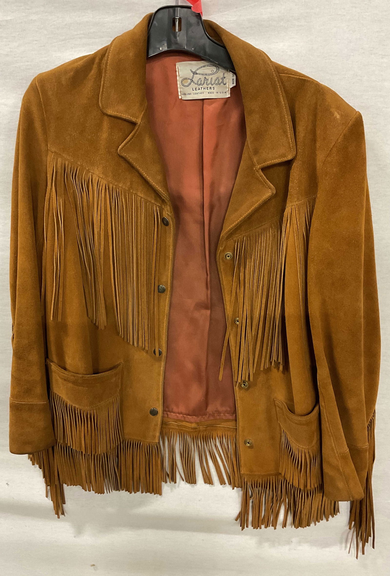 Lariat Brown Leather Western Fringed Jacket USA: Lariat brown leather western fringed jacket. Made in USA. Size 14. 100% genuine leather. Collared jacket. Brown leather fringed trim. Pockets and decorative buttons. Wear consistent with exposure. Pro