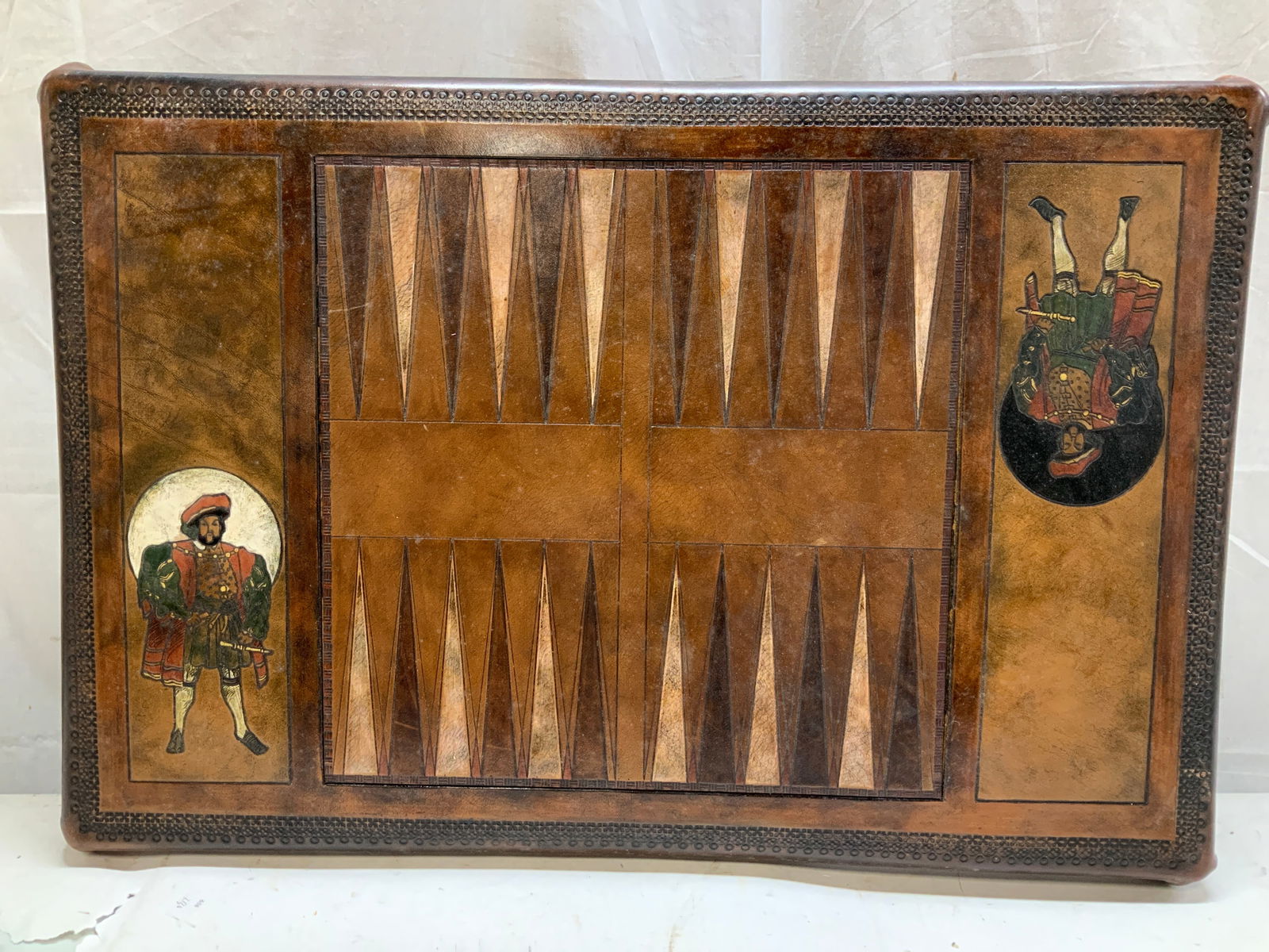 Sgnd Workshop Wales Handmade Backgammon Board 30in: Rectangular backgammon board featuring decorative detailing on border & two Renaissance style male figures. Brown toned. Leather material & handmade. Signed & marked on underside. Reads, WORKSHOP
