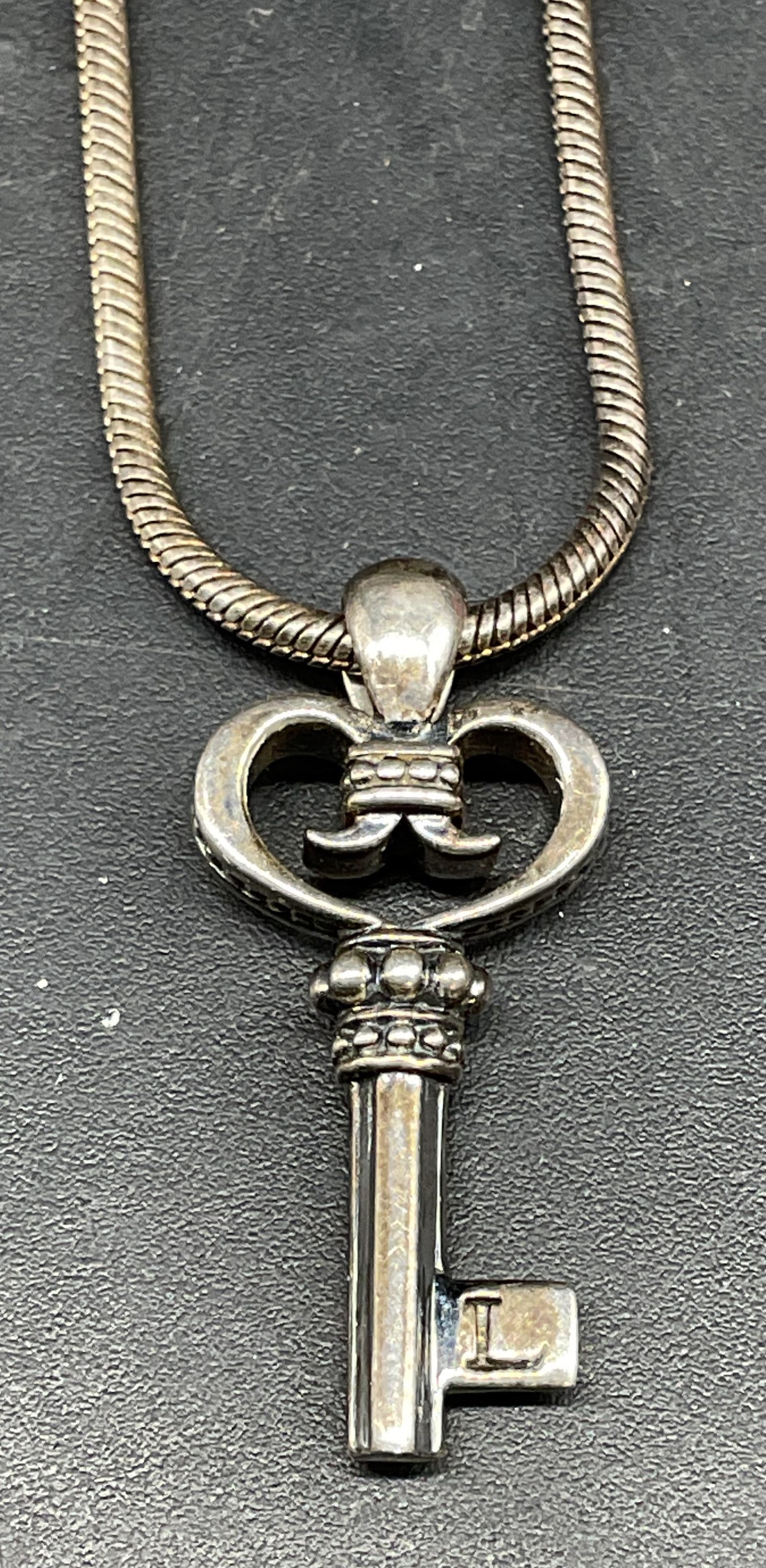 Lagos Sterling Silver Key Pendant Necklace: Signed Lagos sterling silver snake chain necklace with heart and key motif pendant. Drop length approx 9 inches. Pendant measures approx. 1 inch long. Marked sterling. Total weight 10.8 grams. Some sc