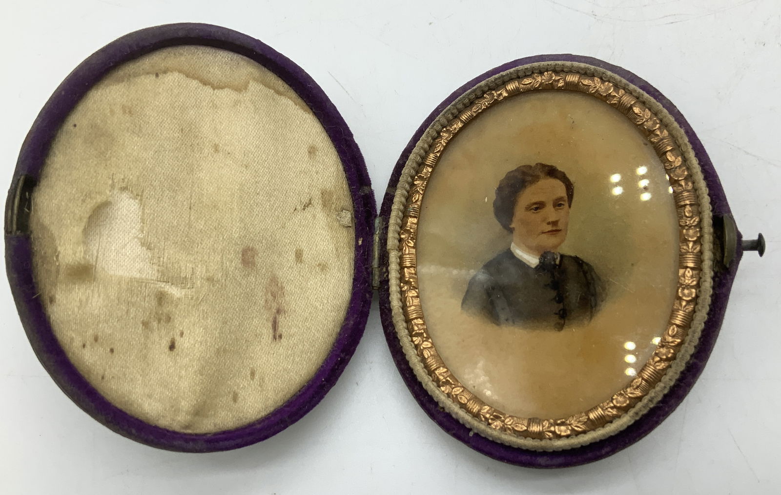 Antique Hand Painted Portrait in Oval Case: Antique oval portrait depicting a woman in a black top. Set under glass & features a decorative gilt border. Case is purple toned. Sold as is. Surface wear consistent to age, use & exposure. Measureme