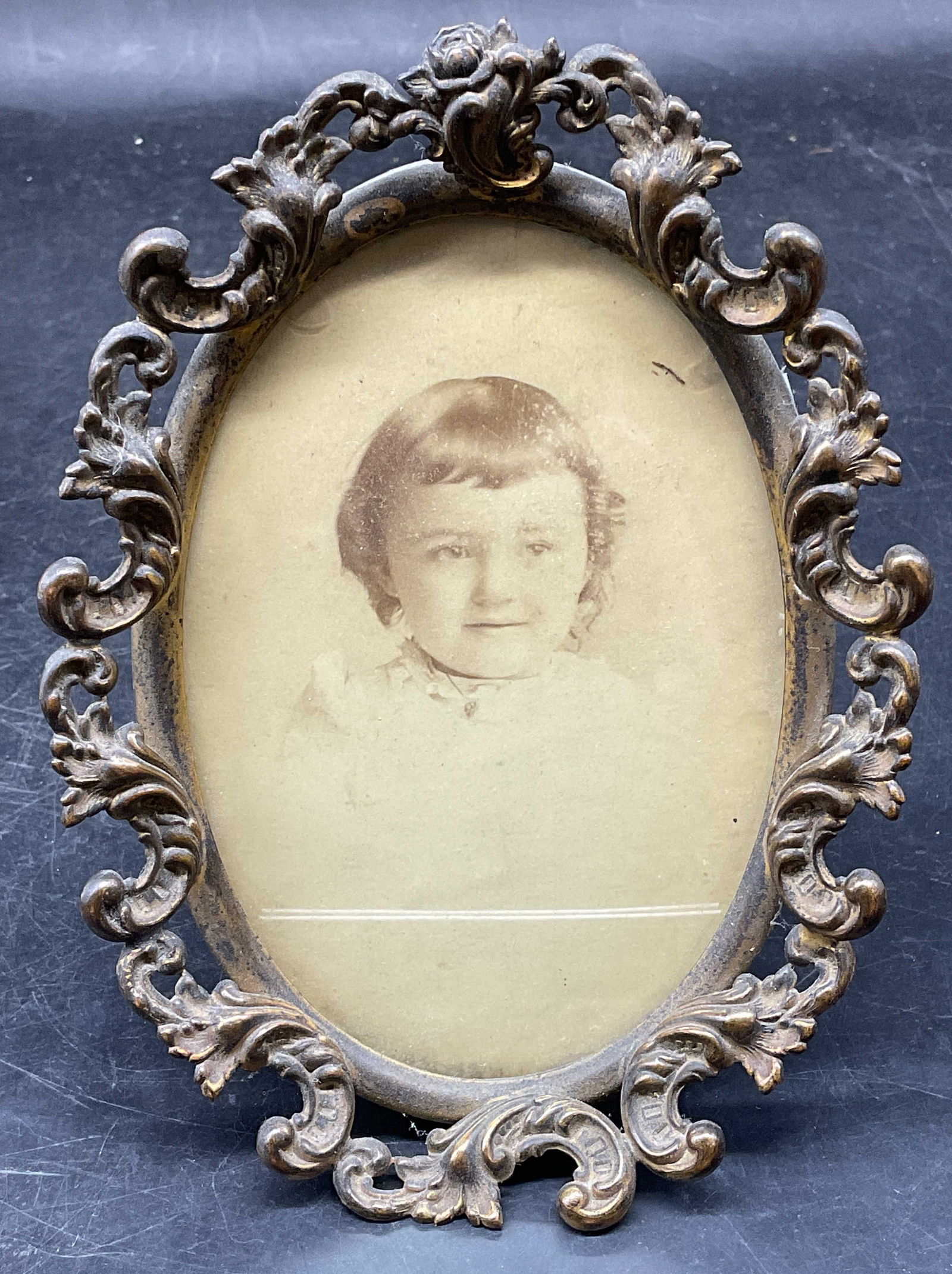 Antique Framed Portrait of Child Photograph: Antique Victorian style metal scroll oval picture frame with Antique sepia photograph. Portrait of a child. Not examined out of frame. Frame measures approx. 6 x 4.25 inches. Some chipping to glass. W