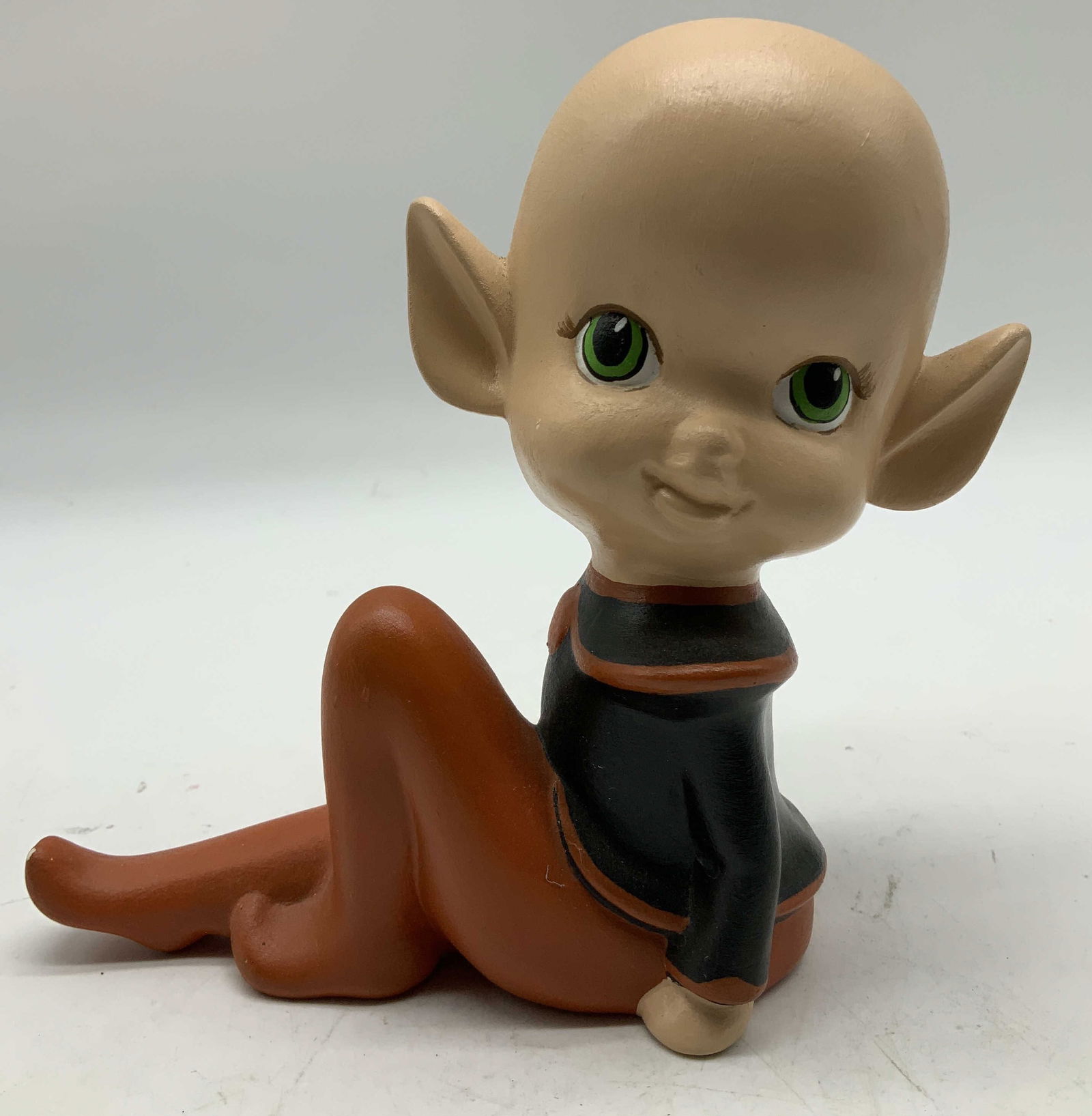 Vntg NM Ceramic Pixie Elf Figurine: Vintage ceramic pixie elf figurine features a bald head with pointed ears, green eyes & in a sitting pose. Signed & marked on underside. Reads, NM 3-73. Surface wear consistent to age, use &
