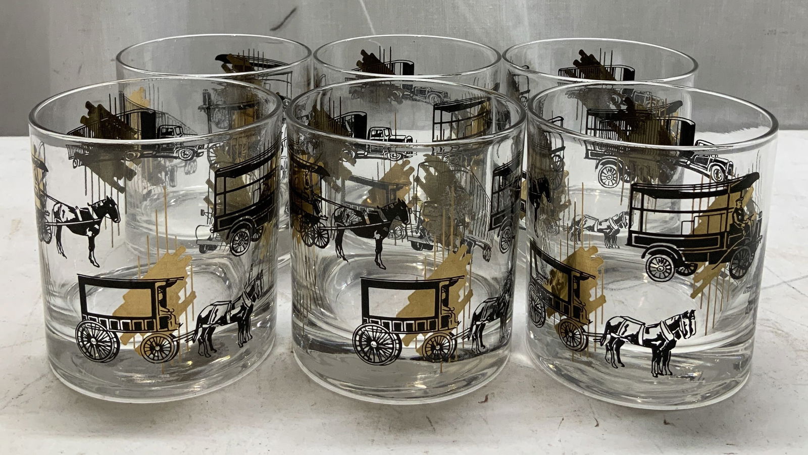 Set 6 Vtg Illustr Gilt Tumbler Glasses: Lot includes, set 6 of tumbler glasses featuring illustrations of horse carriages & trucks. Gilt accents. Surface wear consistent to age, use & exposure. Measurements: length 3.2in x width 3.2in