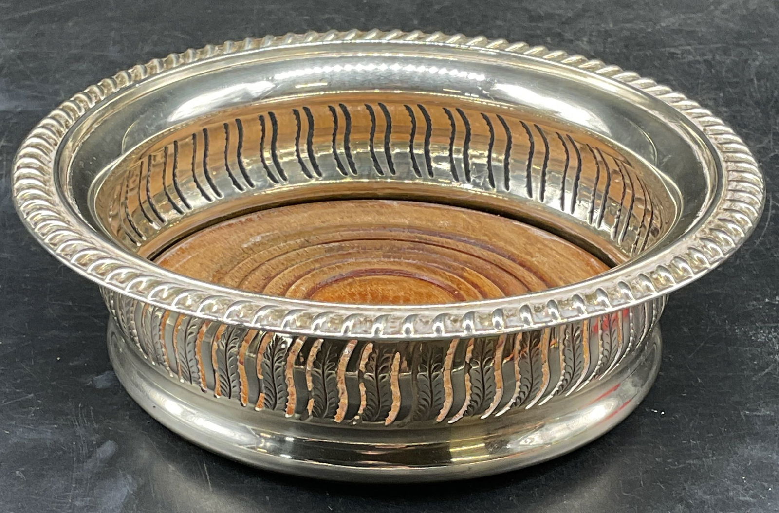 Barker Ellis Silver Plated Wine Coaster, England: Vintage Barker Ellis silver plated win coaster, pierced design with wood base and felted underside. Signed. Made in England. Measures approx. 7.75 x 1.75 inches. Some scratching and patina. Barker Ell