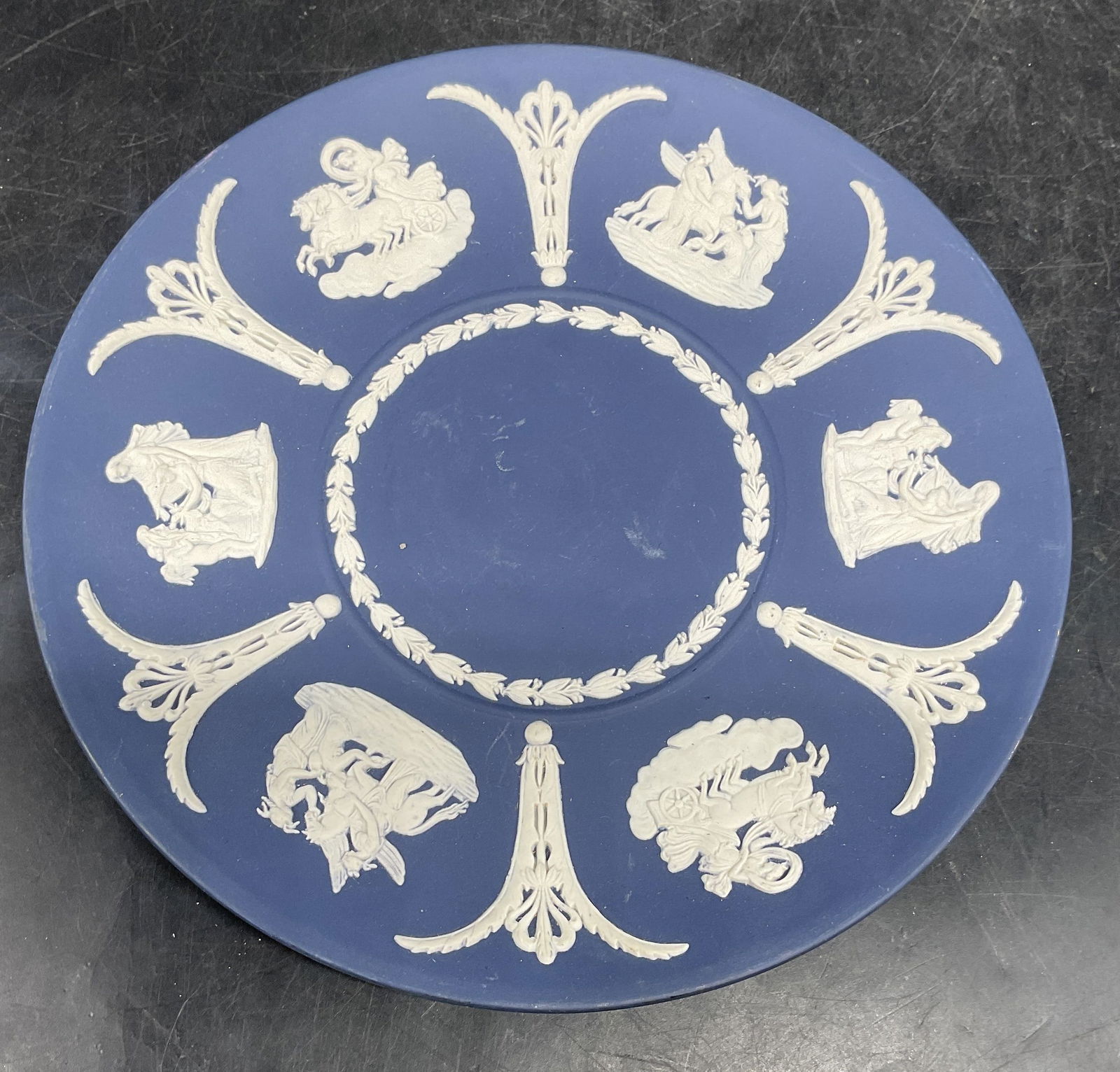 Vintage Wedgwood Blue Jasperware Plate, England: Vintage signed Wedgwood cobalt blue Jasperware plate with white bas relief. Classical figural and scroll design. Measures approx. 8 inches wide. Made in England. Some scratching. Wedgwood plate, Jaspe
