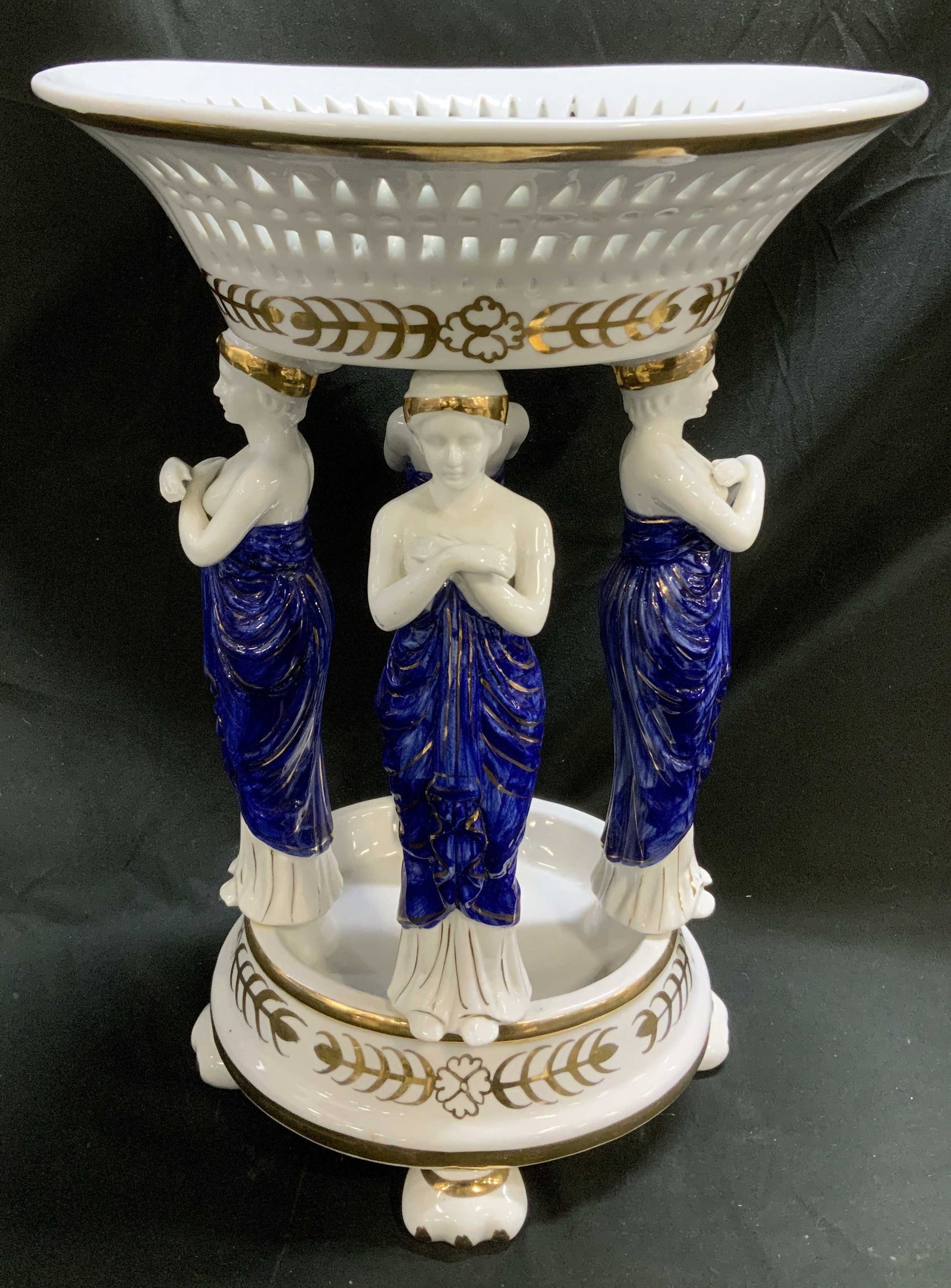Neoclassical Style Gilt & Cobalt Fig Porc Centerpiece: Neoclassical style porcelain centerpiece depicts 4 standing caryatid figures wearing a vibrant cobalt gown with gilt accents. Reticulated basket on top. Centerpiece stands on 4 feet. Extensive gilt ac
