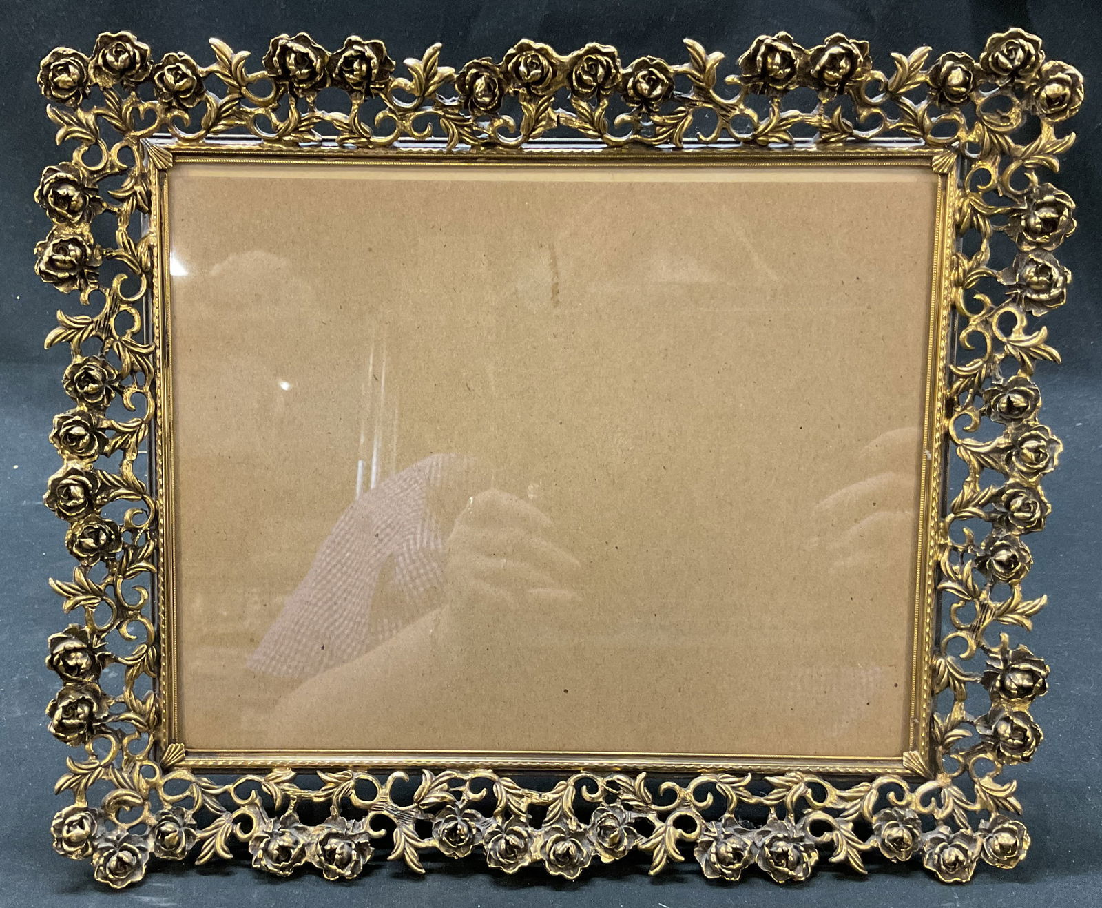 Hollywood Regency Style Brass Picture Frame: Hollywood Regency Style brass picture frame. Rectangular shaped. Ornate scroll motifs. Embossed floral motifs. Gold toned. Measures approx 10 x 12 inches. Surface wear consistent with exposure. Pictur