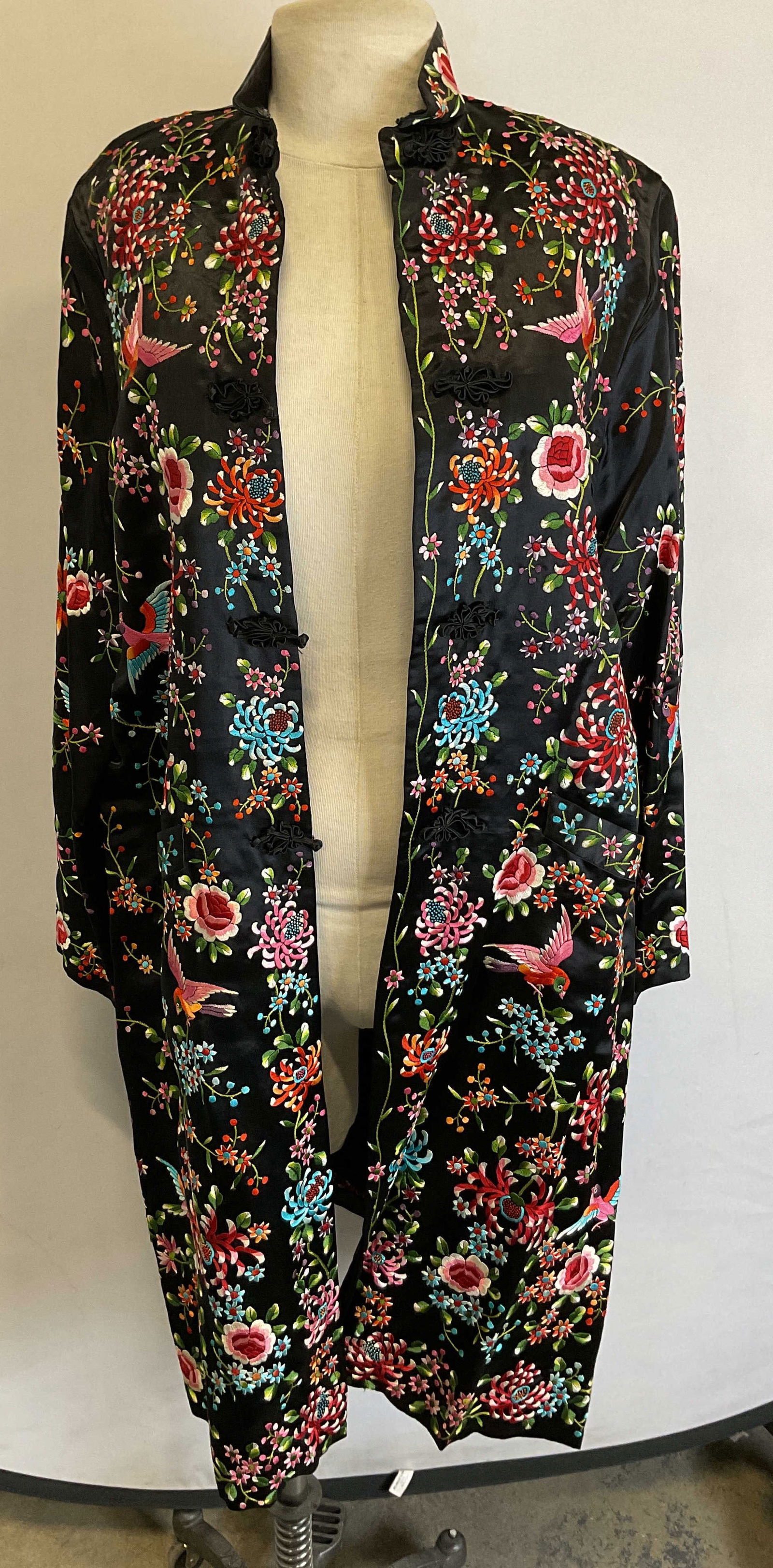Plum Blossom Silk Embroidered Chinese Long Jacket: Plum Blossom silk embroidered Chinese long jacket. Silk material. Embroidered floral and bird motifs in varying colors. Black background. Collared jacket. Decorative traditional frog closures. Front p