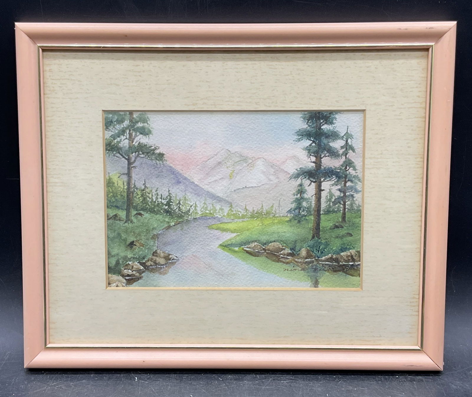 Framed Signed Landscape Watercolor Painting: Framed and matted watercolor painting. Signed lower right, illegible. Landscape with stream and mountains. Pink frame. Not examined out of frame. Frame measures approx 8.75 x 10.75 inches. Wear includ