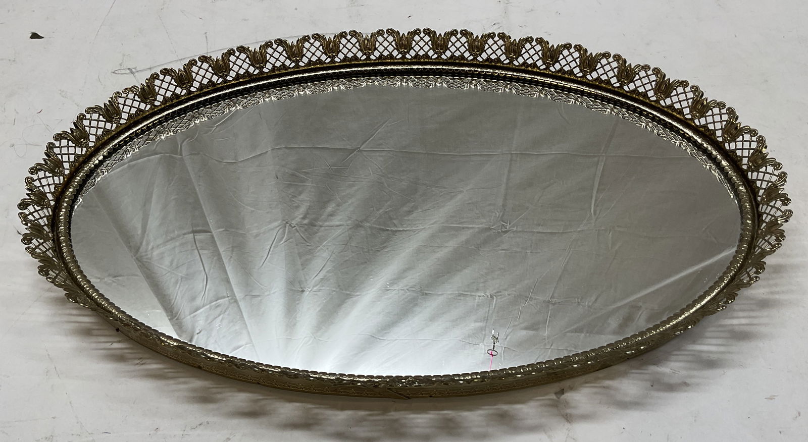 Vintage Gold Toned Metal Oval Vanity Mirror Tray: Vintage gold toned metal oval vanity mirror tray. Gold toned metal border with ornate scroll and floral motifs. Oval shaped tray with a mirrored center. Measures approx 13 x 21 inches. Surface wear co