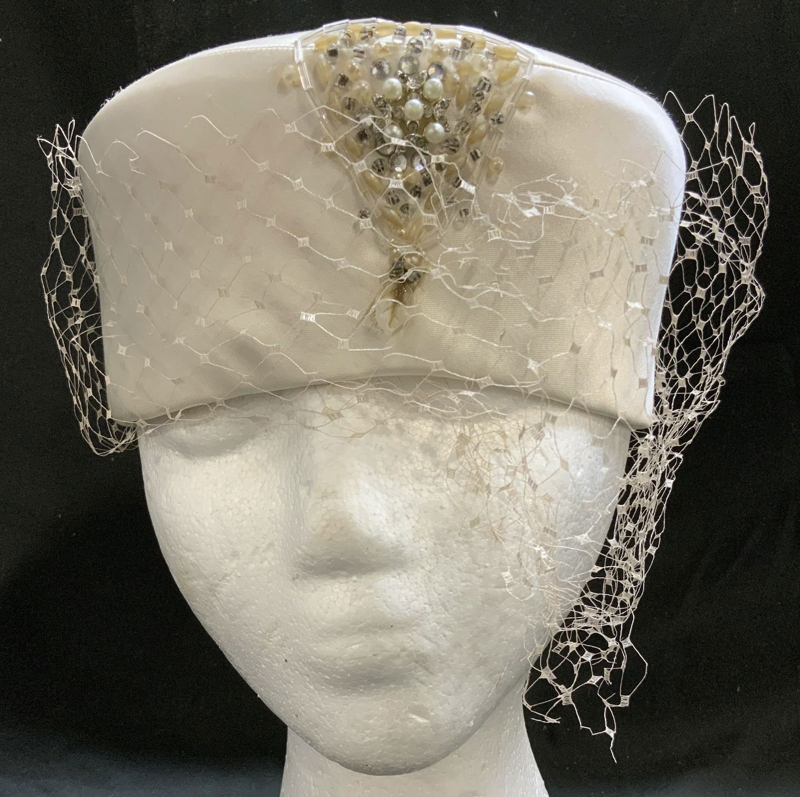 Vntg Aileen Zollinger White Pillbox Style Hat: Vintage Aileen Zollinger white pillbox style hat features a veil accent that covers tops & sides of hat. Front of hat features an embellishment made of faux pearls & rhinestone accents. Signed & marke