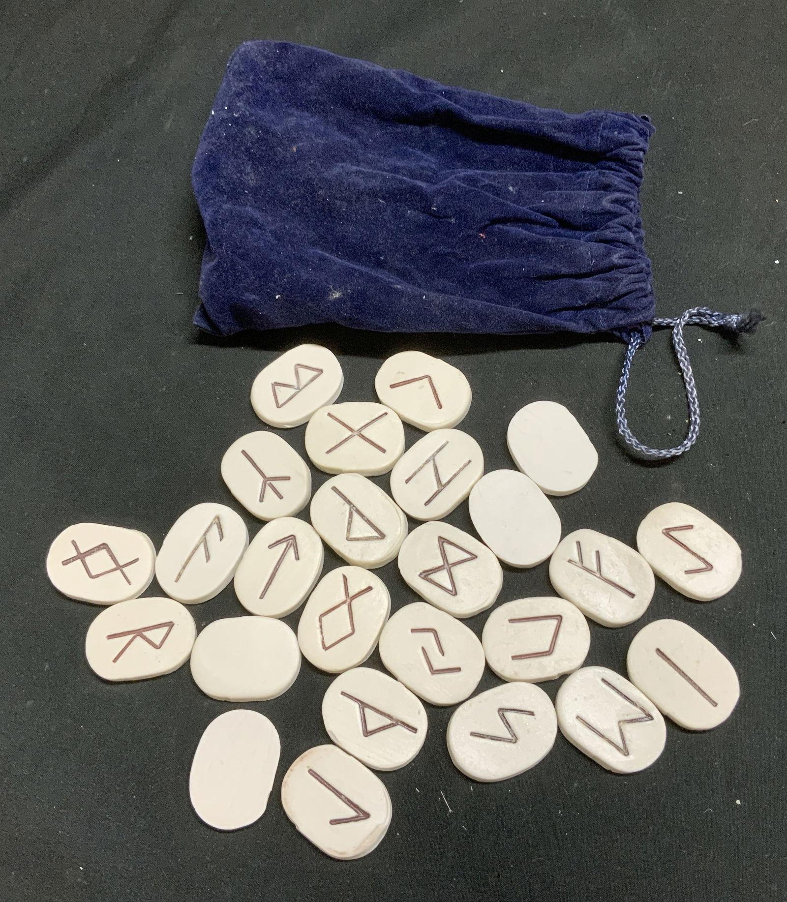 Lot 26 Ceramic Runes & Drawstring Pouch: Lot includes, 25 ceramic runes featuring ancient alphabetical symbols & navy drawstring pouch. Lot is sold as is. Surface wear consistent to age, use & exposure. Property of Upper East Side