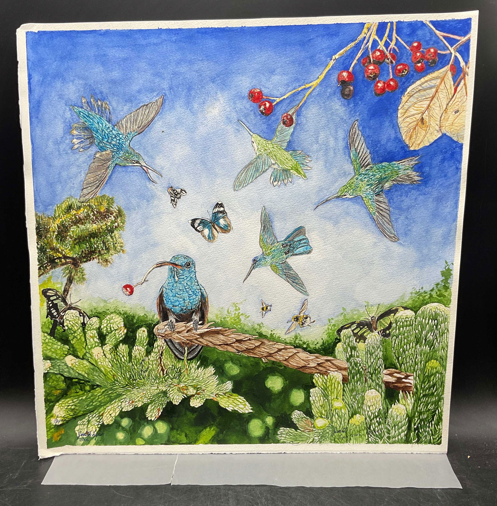 Judith Lynn Hummingbirds Watercolor Painting: Watercolor painting on paper. Signed Judith Lynn. Humming With Berry. Hummingbirds. Measures approx 16.75 x 16.5 inches. Some wear consistent with exposure. Property of opera singers estate from