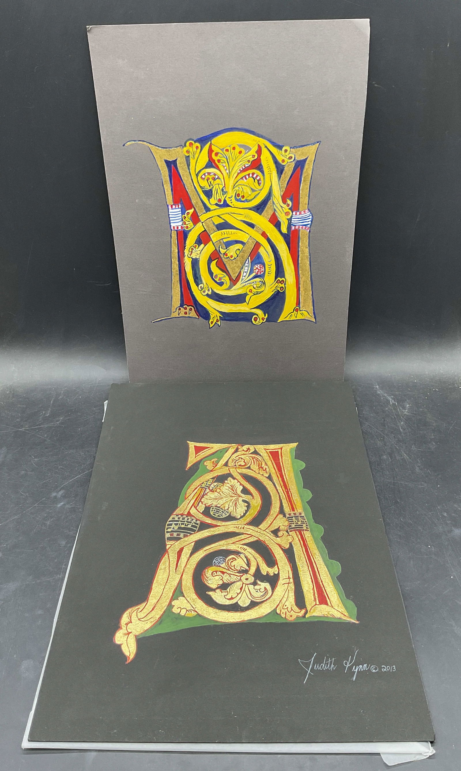 2 Judith Lynn Gothic Letter A M Gilt Watercolors: Lot of 2 watercolor, ink, and gold leaf paintings on board. One signed Judith Lynn. Gothic Letter A and M. Larger measures approx. 16 x 11inches. Some wear consistent with exposure. Some residue