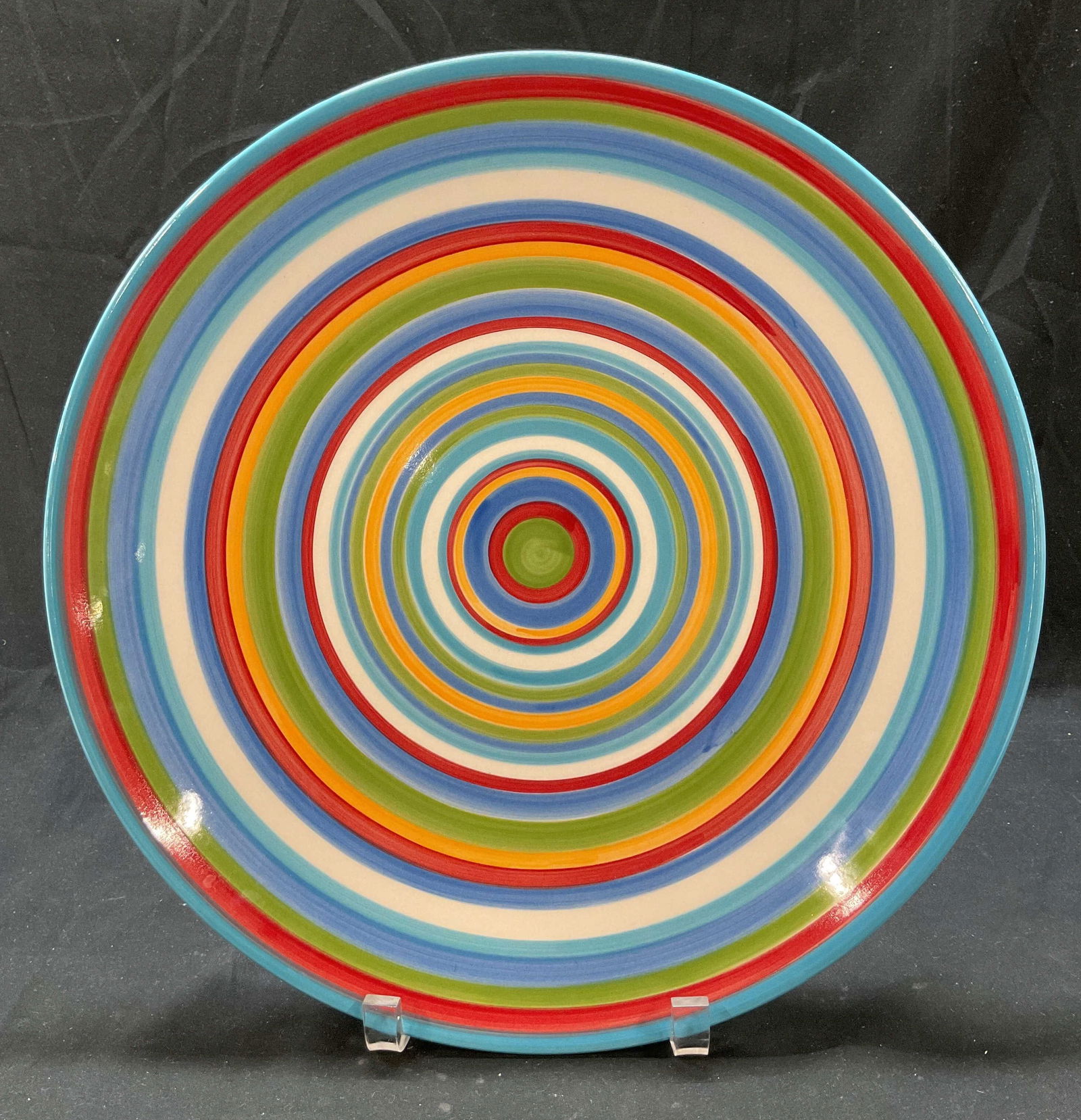 Home Multicolored Ceramic Serving Plate: Home multicolored hand painted ceramic serving plate. Circular bands hand painted in blue, red, green, white, and orange. Target style design. Measures approx 14 inches in diameter. Surface wear