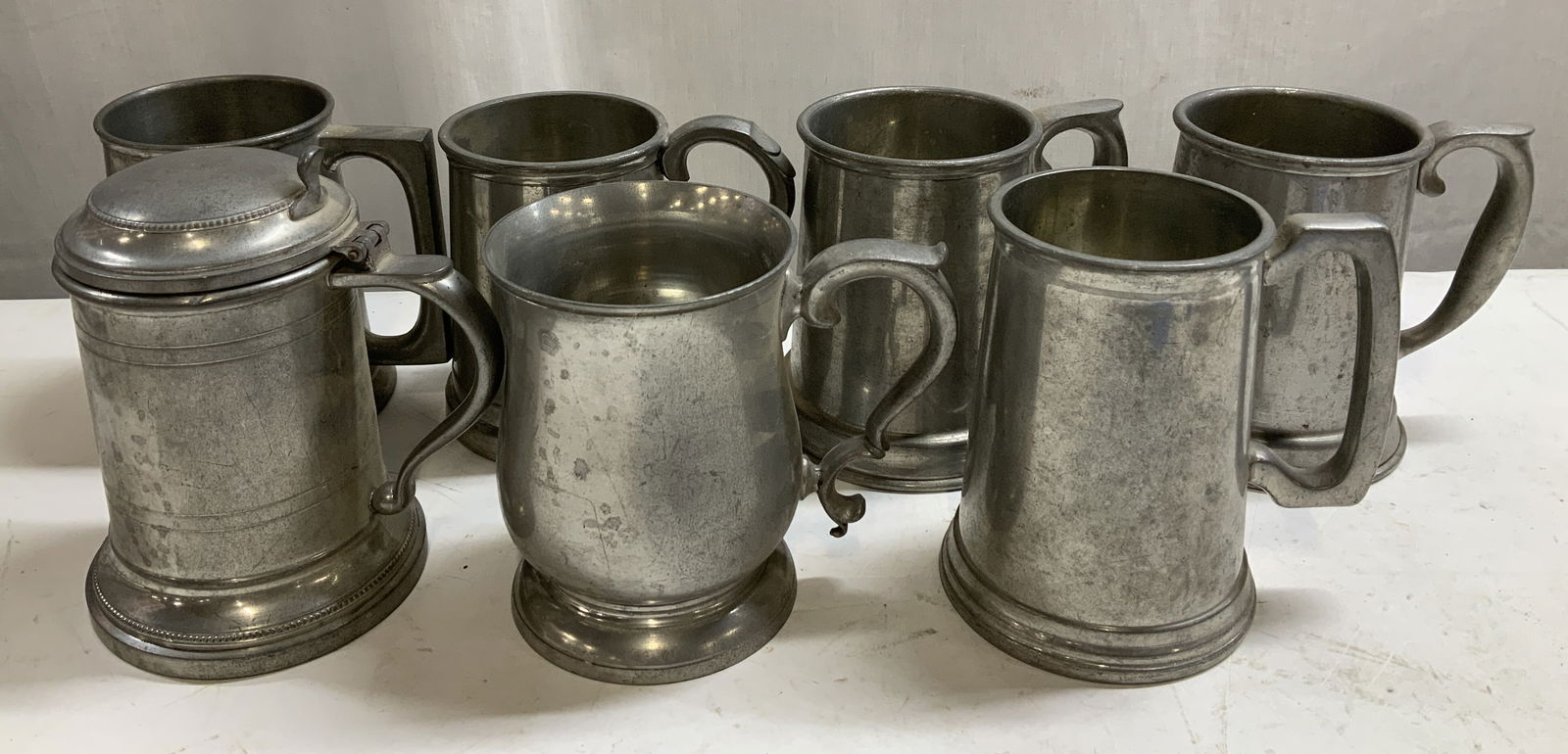 Lot 7 Pewter Tankards WORCESTER ENGLAND+: Lot includes, 1 pewter tankard with lid & 6 pewter tankards with ornate handles. Assorted brands. Signed & marked on underside. Reads, WILLIAMSBURG STIEFF PEWTER, WORCESTER SILVER CO. MADE IN ENGLAND,