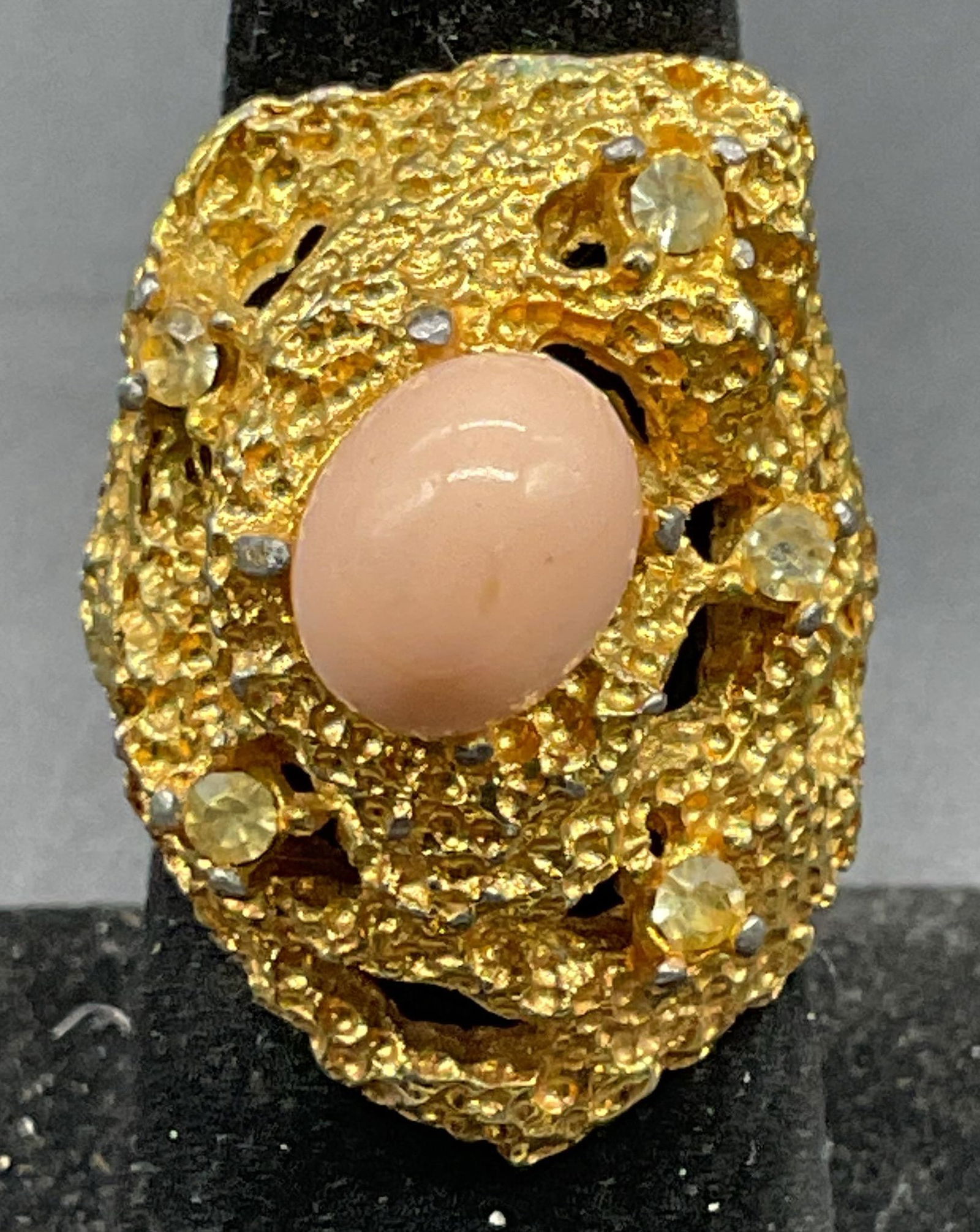 Vintage Vogue Gold Tone Pink Cocktail Ring: Vintage signed Vogue gold tone cocktail ring with pink faux cabochon and crystals. Adjustable band. Setting measures approx. 1.25 inches wide. Some scratching. Jewelry, estate jewelry, costume