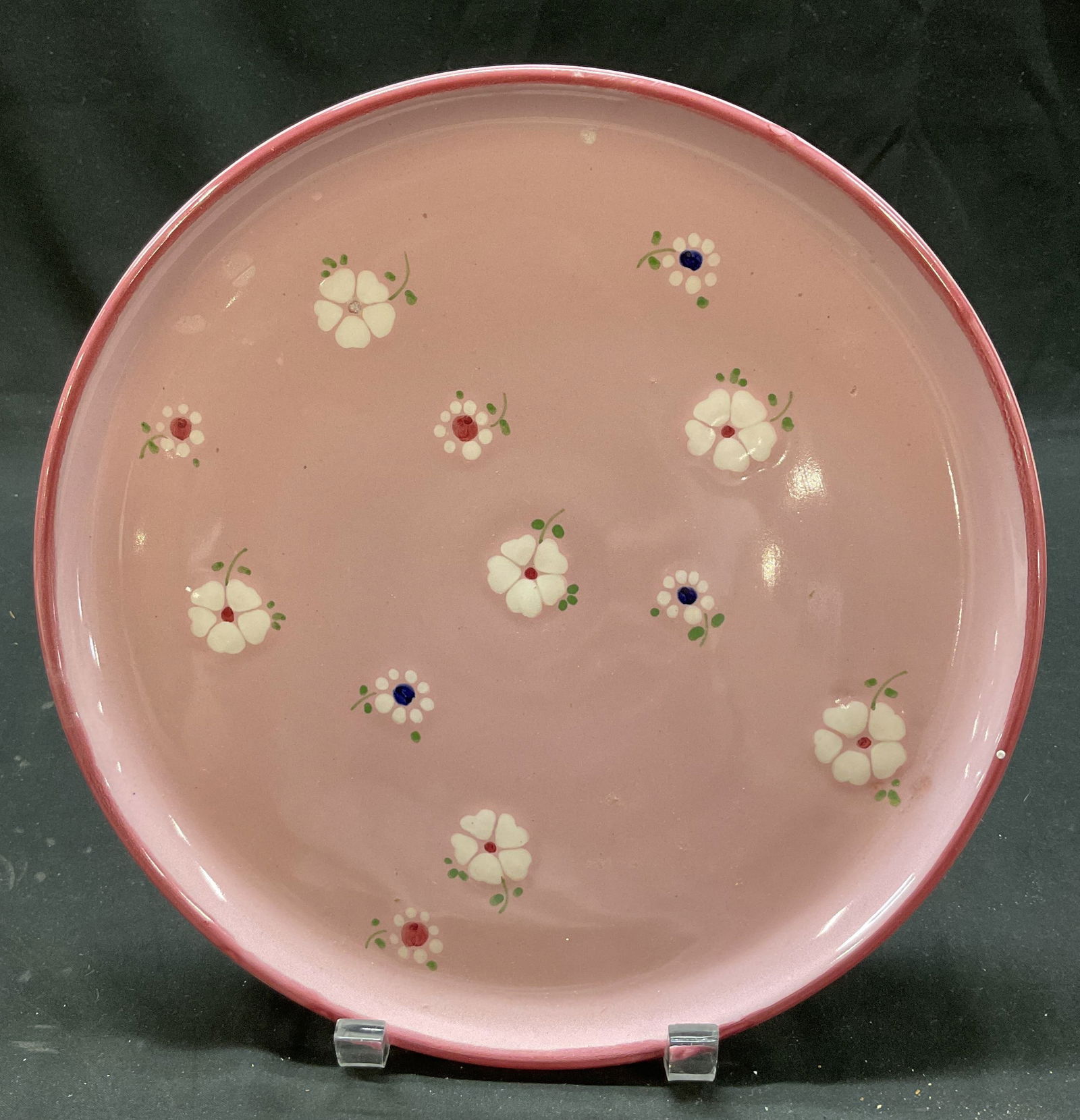 Vintage Pink Ceramic Floral Plate Italy: Vintage pink ceramic floral plate. Signed Italy on underside. Round plate. Pink with hand painted floral motifs in white, green, pink, and blue. Measures approx 10.5 inches in diameter. Surface wear c