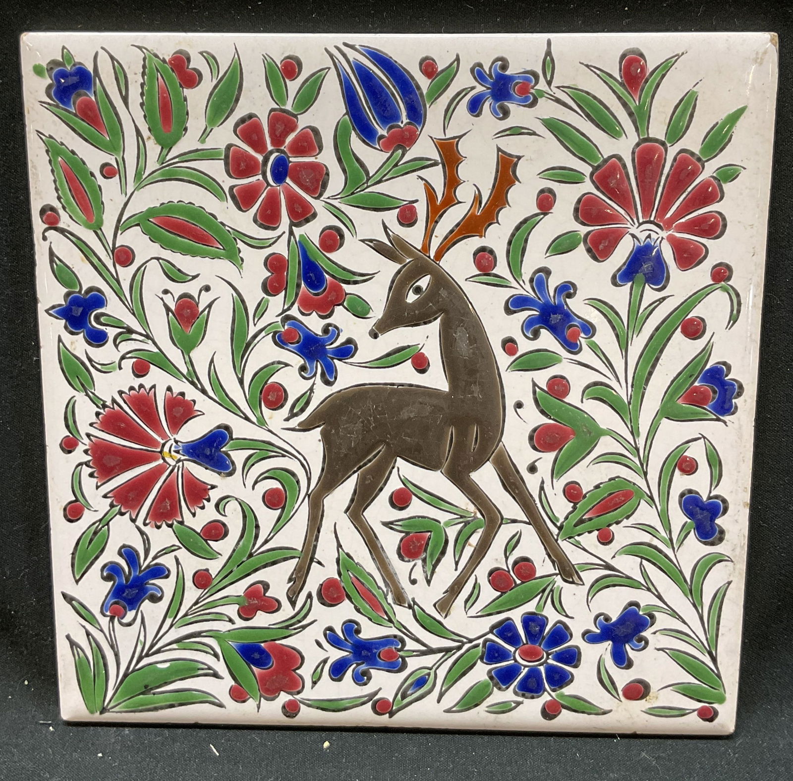 Nassos Keramik Ceramic Deer Deco Tile: Nassos Keramik ceramic deer decorative tile. Marked on underside, reads Hand Made By Nassos Keramik Paradiso Rodos Ellas. Square tile. Deer motif surround by floral motifs. Hand painted in brown, blue