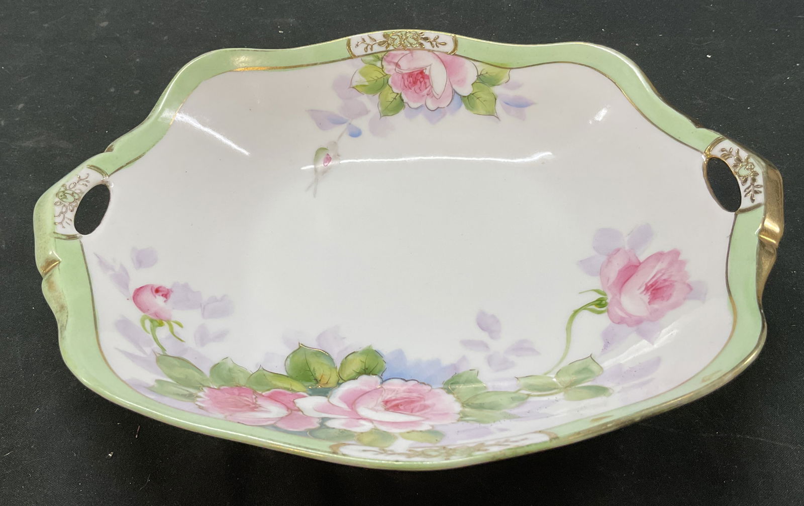 Vintage Hand Painted Porcelain Dish Nippon: Vintage hand painted porcelain dish. Marked on underside, reads Hand Painted Nippon. Two small cut out handles. Hand painted floral motifs. Gilt decoration. Purple, green, and pink. Measures approx 8