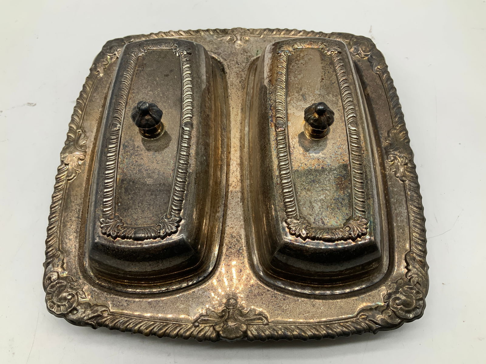 Vtg Ornate Silver Plated Double Butter Dish: Vintage silver plated double butter dish features two individual compartments, each with a decorative lid. Ornate border. Signed & marked on underside. Reads, SILVERPLATE. Surface wear consistent
