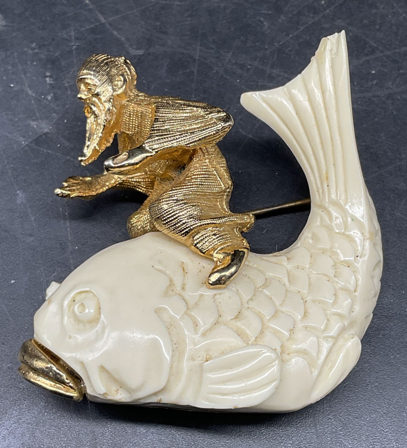 Gold Tone White Figural Fish Brooch: Gold tone and white resin man riding fish motif brooch. Measures approx. 1.75 x 1.75 inches. Some chips and scratching. Jewelry, estate jewelry, costume jewelry, cocktail jewelry, fashion jewelry, acc