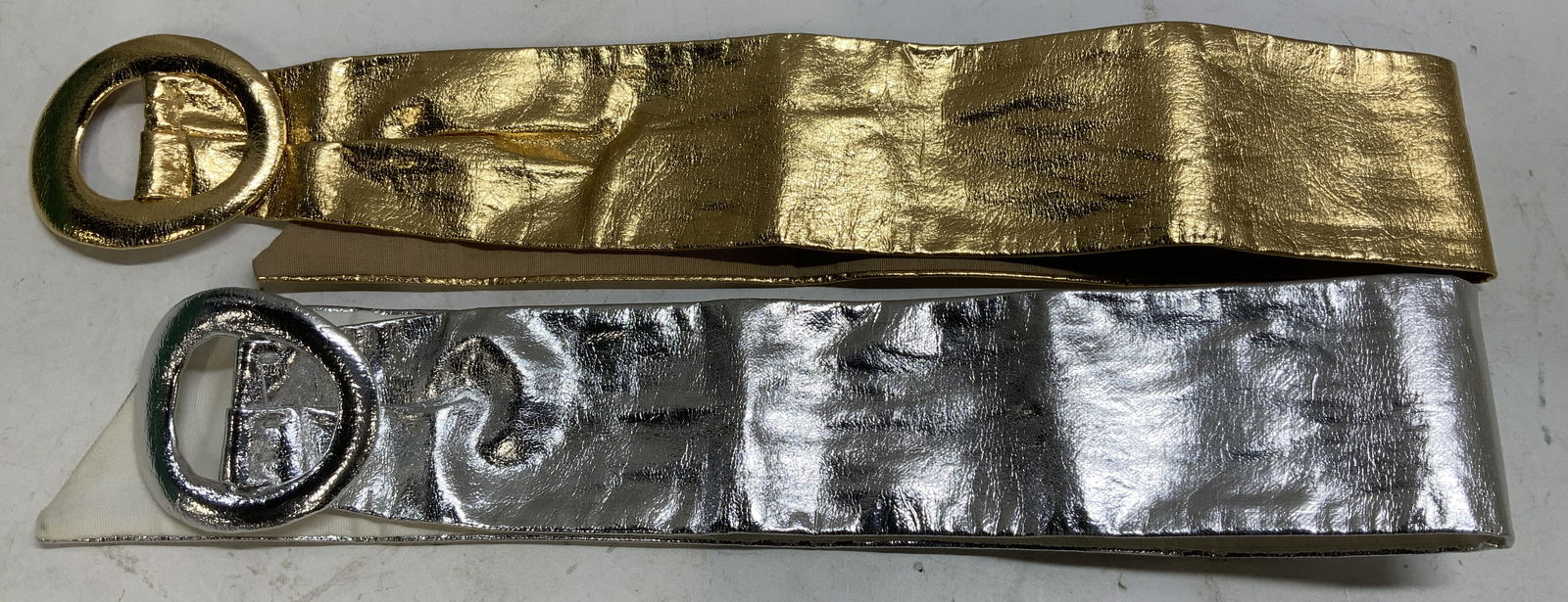 Lot 2 Vtg Garay Metallic & Gold Toned Belts: Lot 2 includes, 1 metallic & gold toned decorative belt. Features a large round buckle. Fabric material on underside. Signed & marked. Reads, GARAY. Surface wear consistent to age, use & exposure. Mea