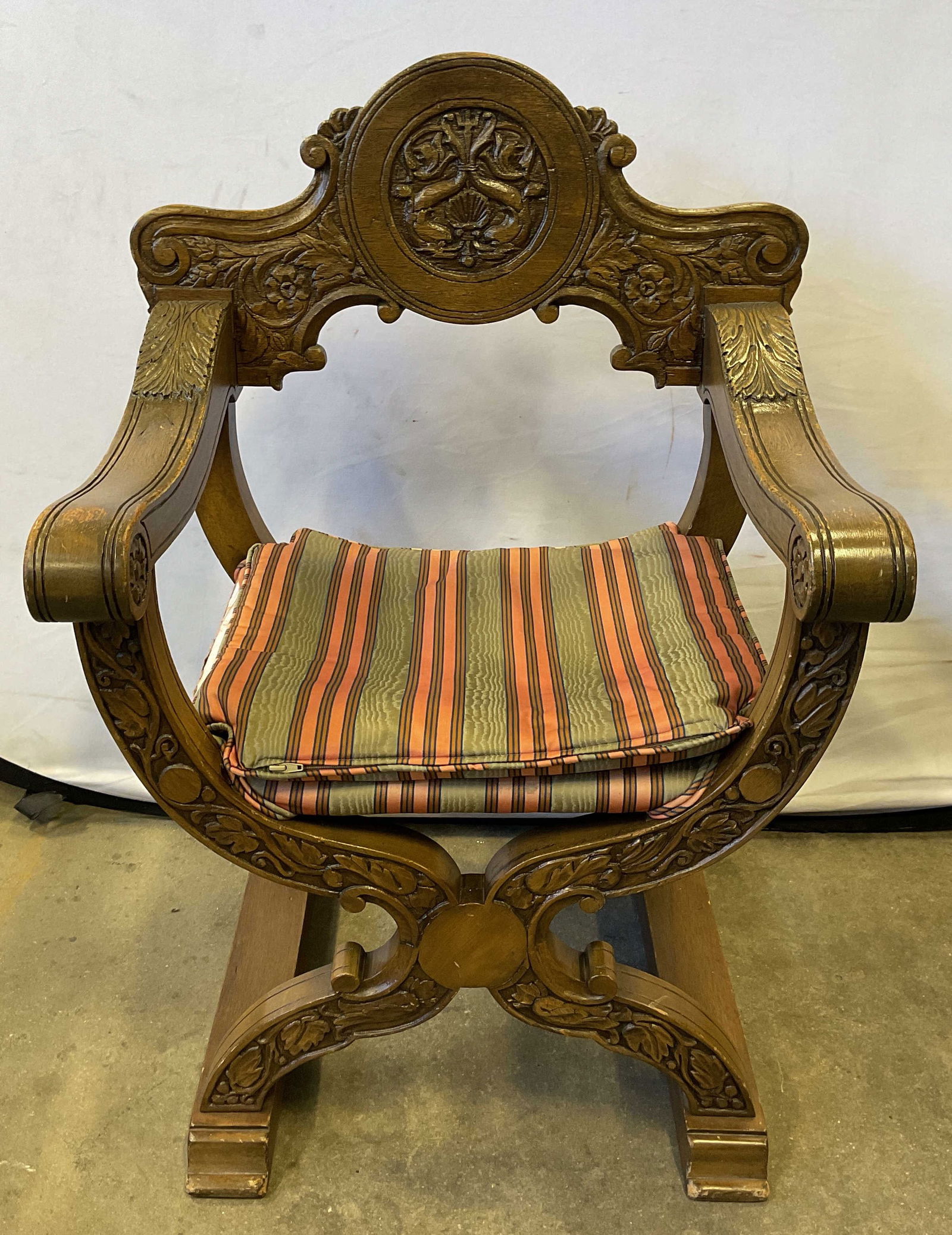 Renaissance Revival Style Savonarola Chair: Renaissance Revival Savonarola style armchair. Chair does not fold. Curved x frame. Ornate carved floral scroll details. Upholstered set and cushion in green and red stripe. Measures approx. 24.5