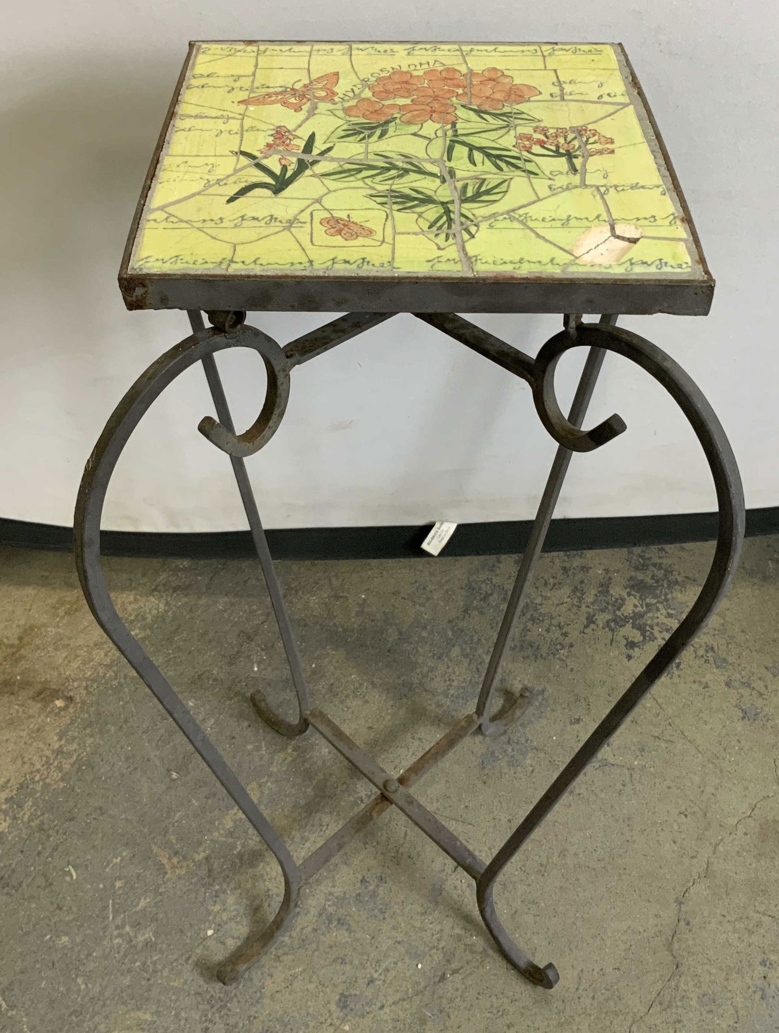 Vtg Wrought Iron Plant Stand 21in: Vintage wrought iron plant stand featuring a square ceramic top with floral motifs. Green & orange toned. Tile has lettering, Hydrangea. Surface wear consistent to age, use & exposure.